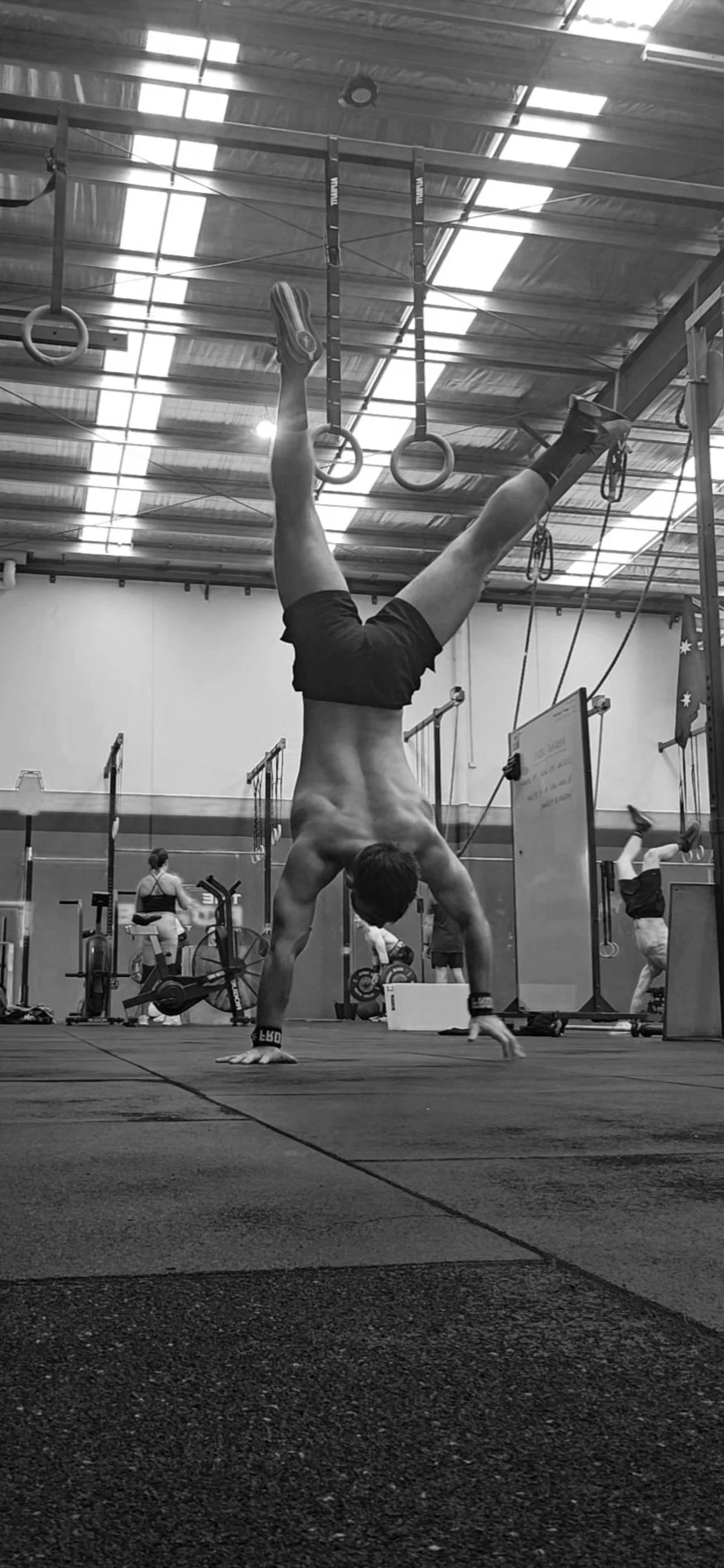 Man performing a handstand at a gym with gymnastic rings hanging from the ceiling.