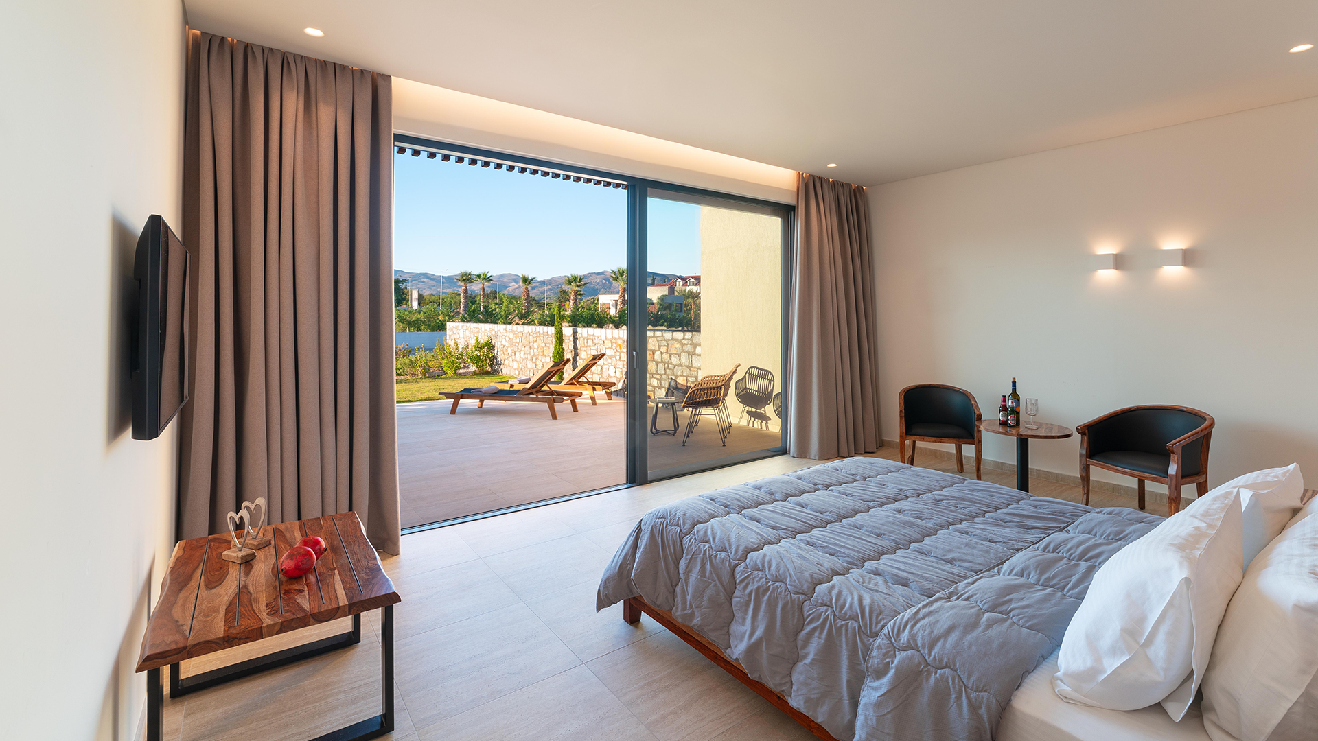 Rhodes Suite room, sitting area, and large sliding glass door leading to balcony with outdoor lounge chairs and scenic views