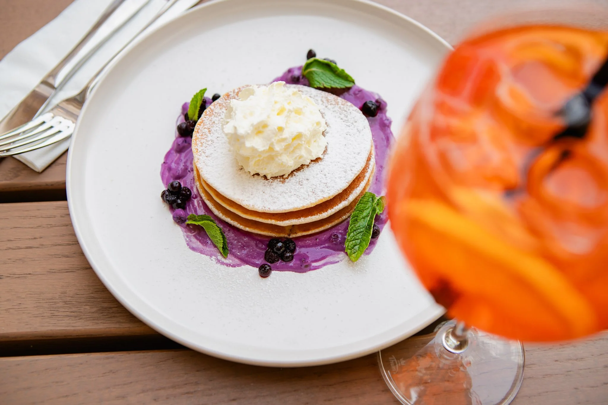 Blueberry pancake topped with whipped cream, Aperol Spritz.