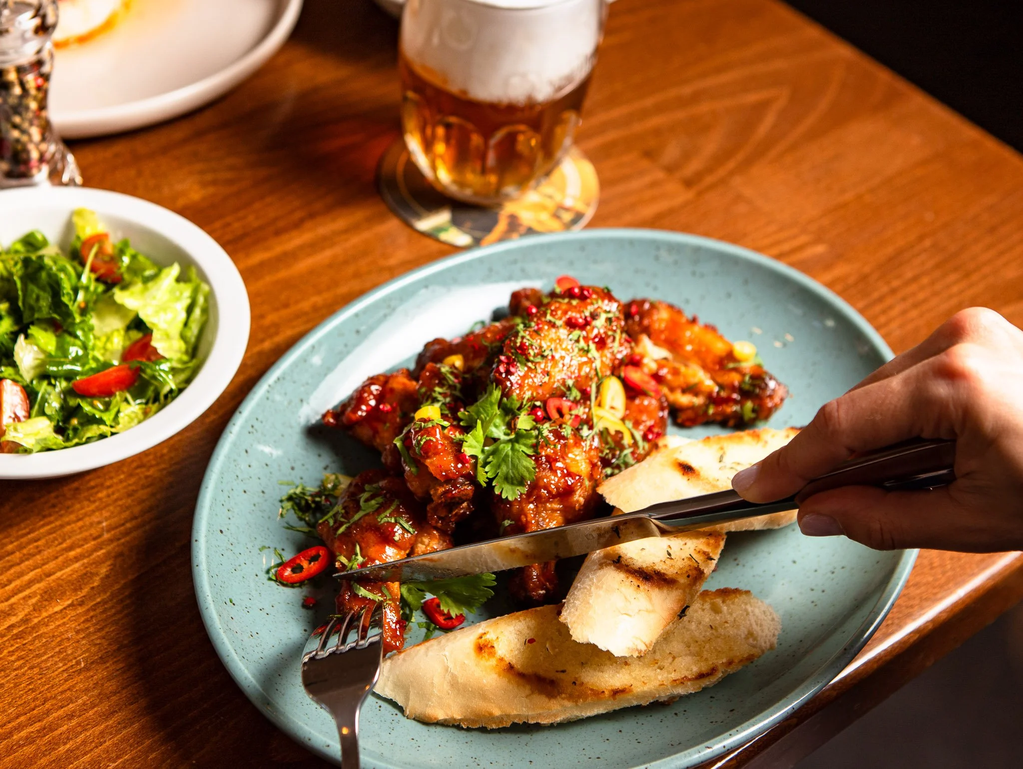 Chicken wings garnished with cilantro and sliced red chili peppers, served with bread. A side salad with lettuce, tomatoes. A glass of Czech beer.