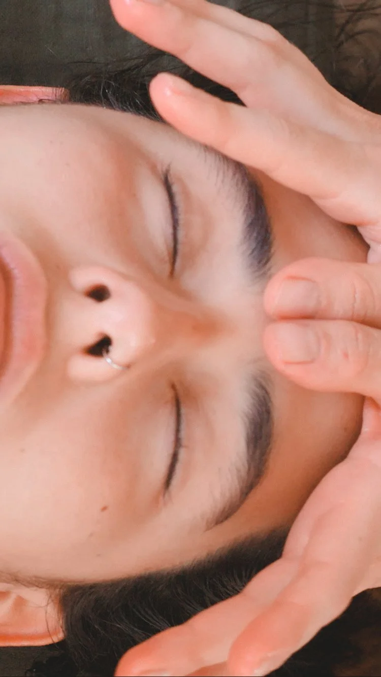 Hands gently massaging a forehead during a Kobido facial treatment.