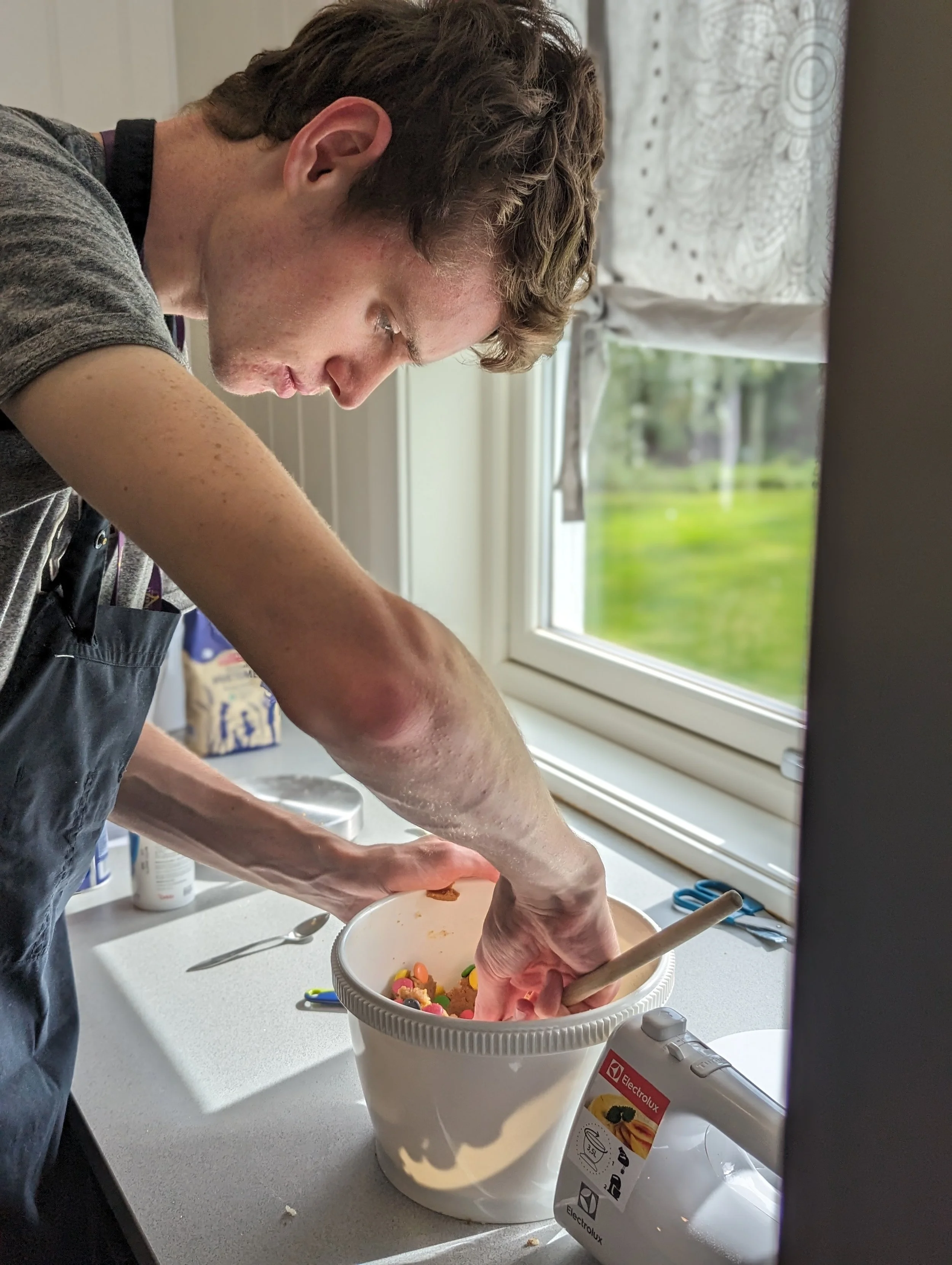 En person baker kaker sammen med noen andre i et kjøkken, med en bowl full av ingredienser og omgitt av kjøkkenutstyr.