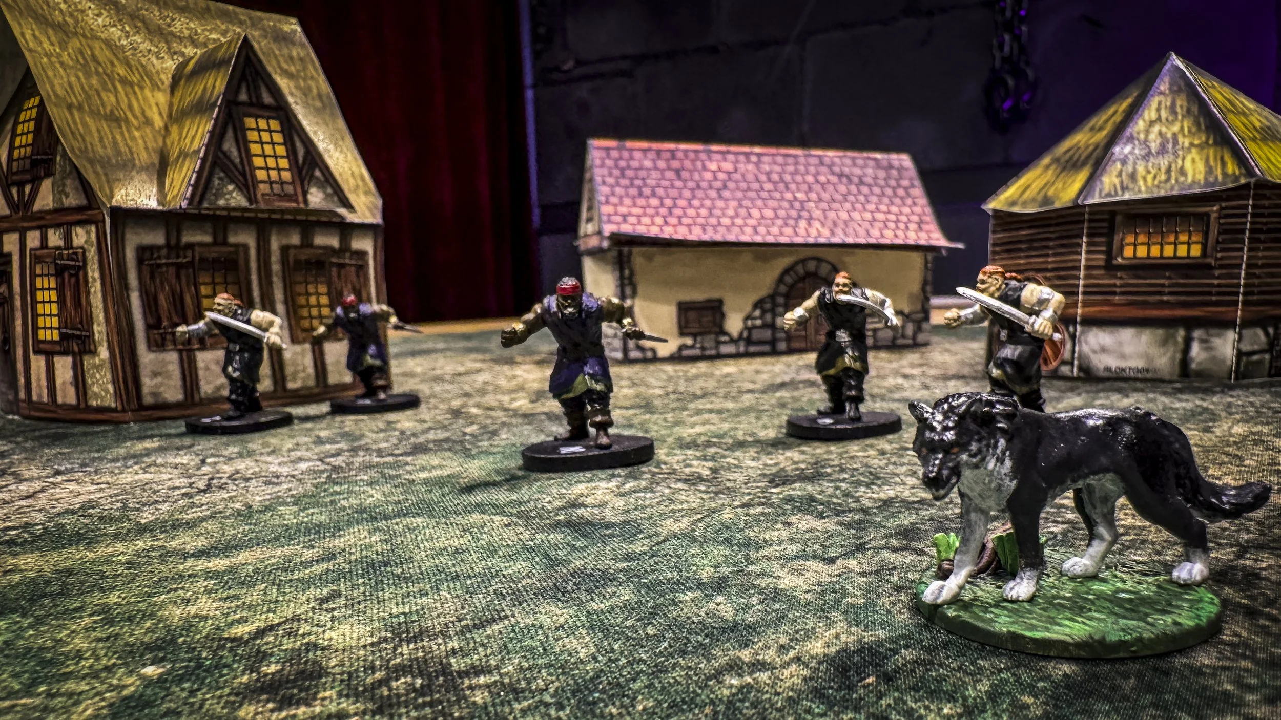 Miniature figurfigurer av krigere med sverd, et stort svart og hvitt hundestatu på en grønn plattform, omgitt av trer og hytter i en landsby.