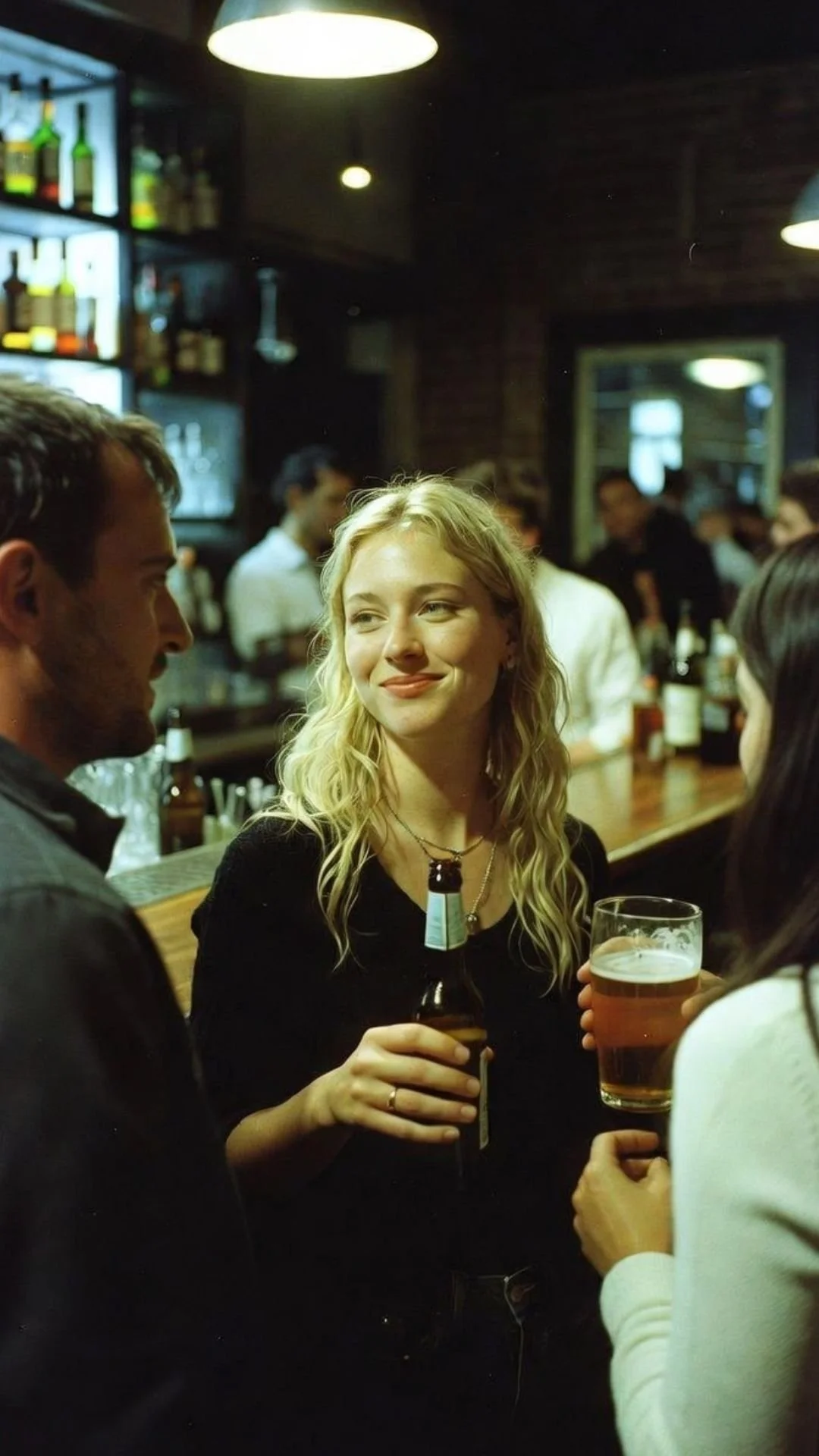 A group of people socializing at a bar, with a woman holding a beer bottle and a woman holding a glass of beer in the foreground.