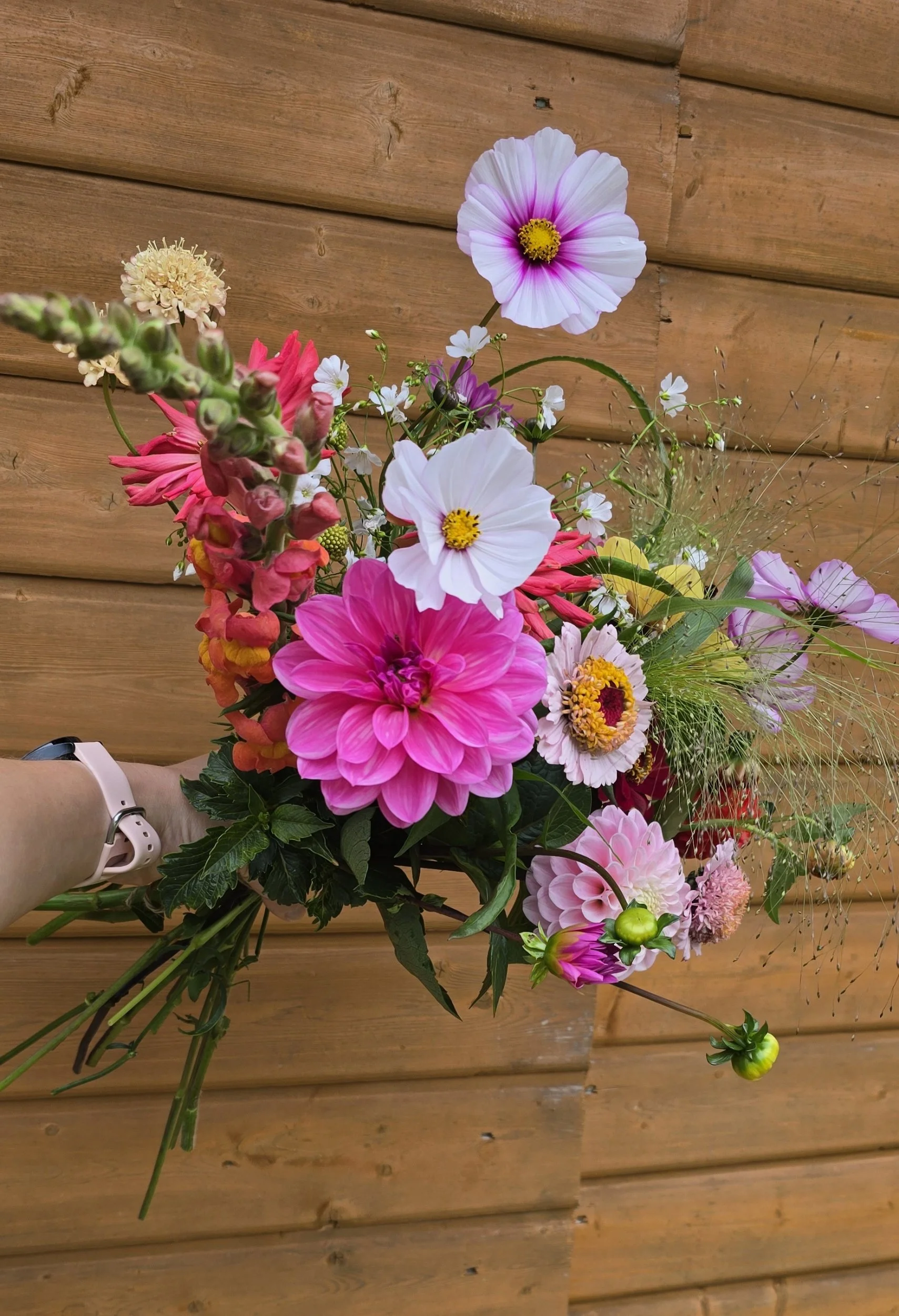 Ellie holds a bouquet of seasonal flowers in front of a wooden building