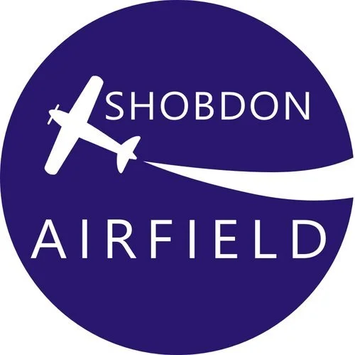 Logo with a white airplane silhouette and the words 'SHOBDON AIRFIELD' on a dark blue circular background.