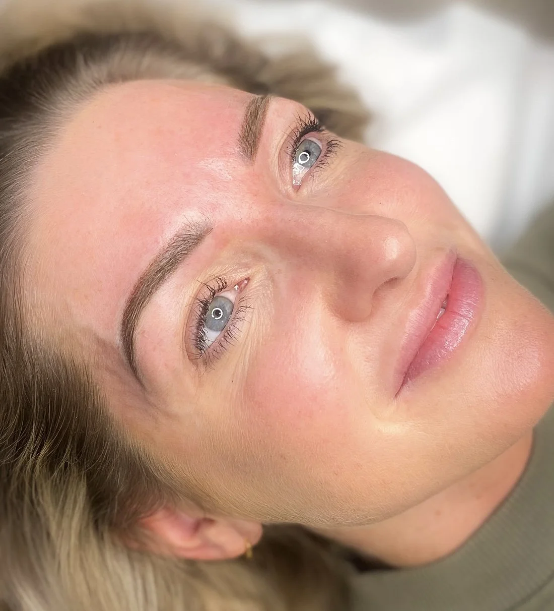 A close-up of a woman's face with light skin, blue eyes, and blonde hair, lying down and looking up.