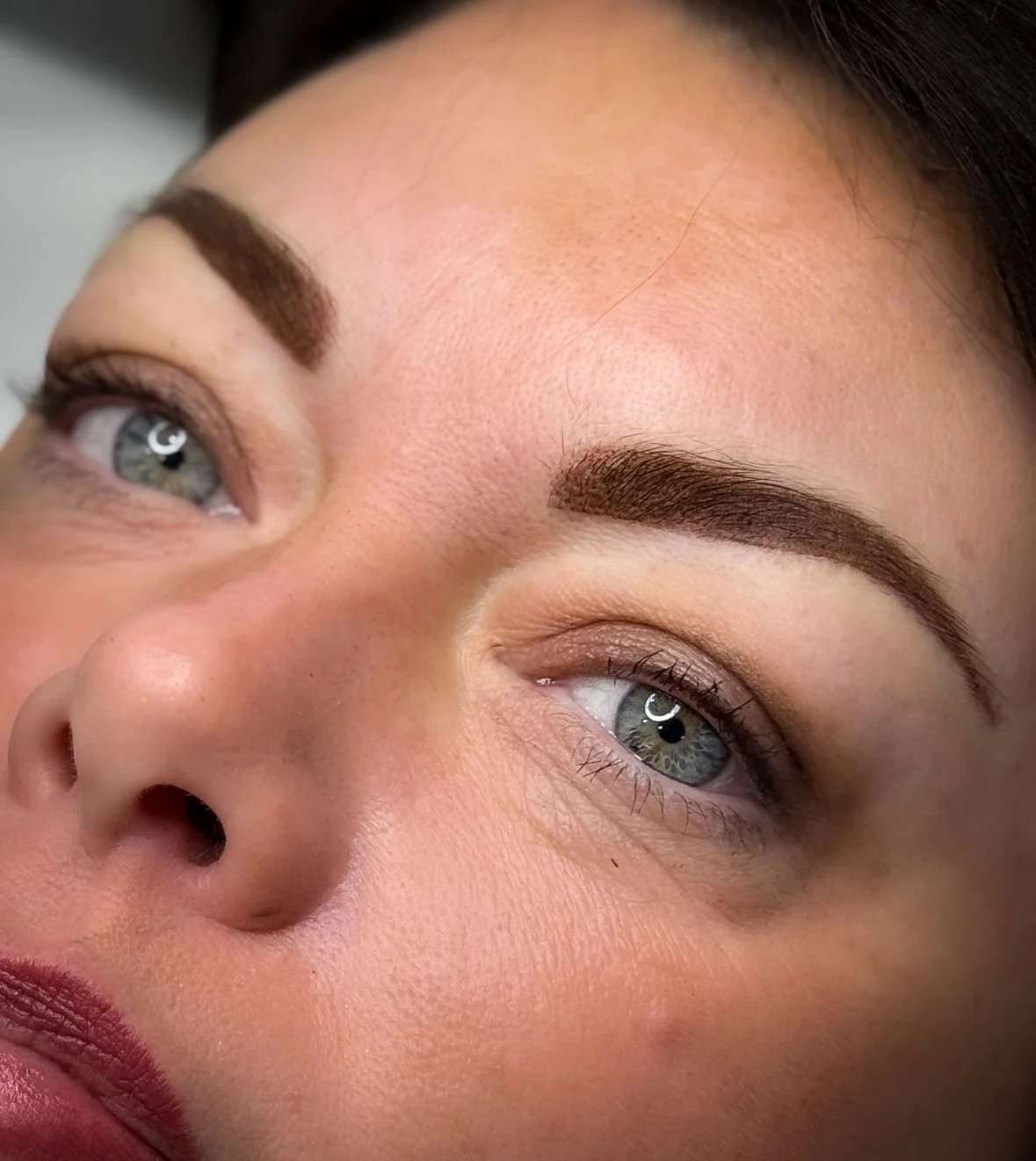 Close-up of a woman's face showing her eyes, eyebrows, and part of her nose. She has light skin, blue eyes, and dark eyebrows.