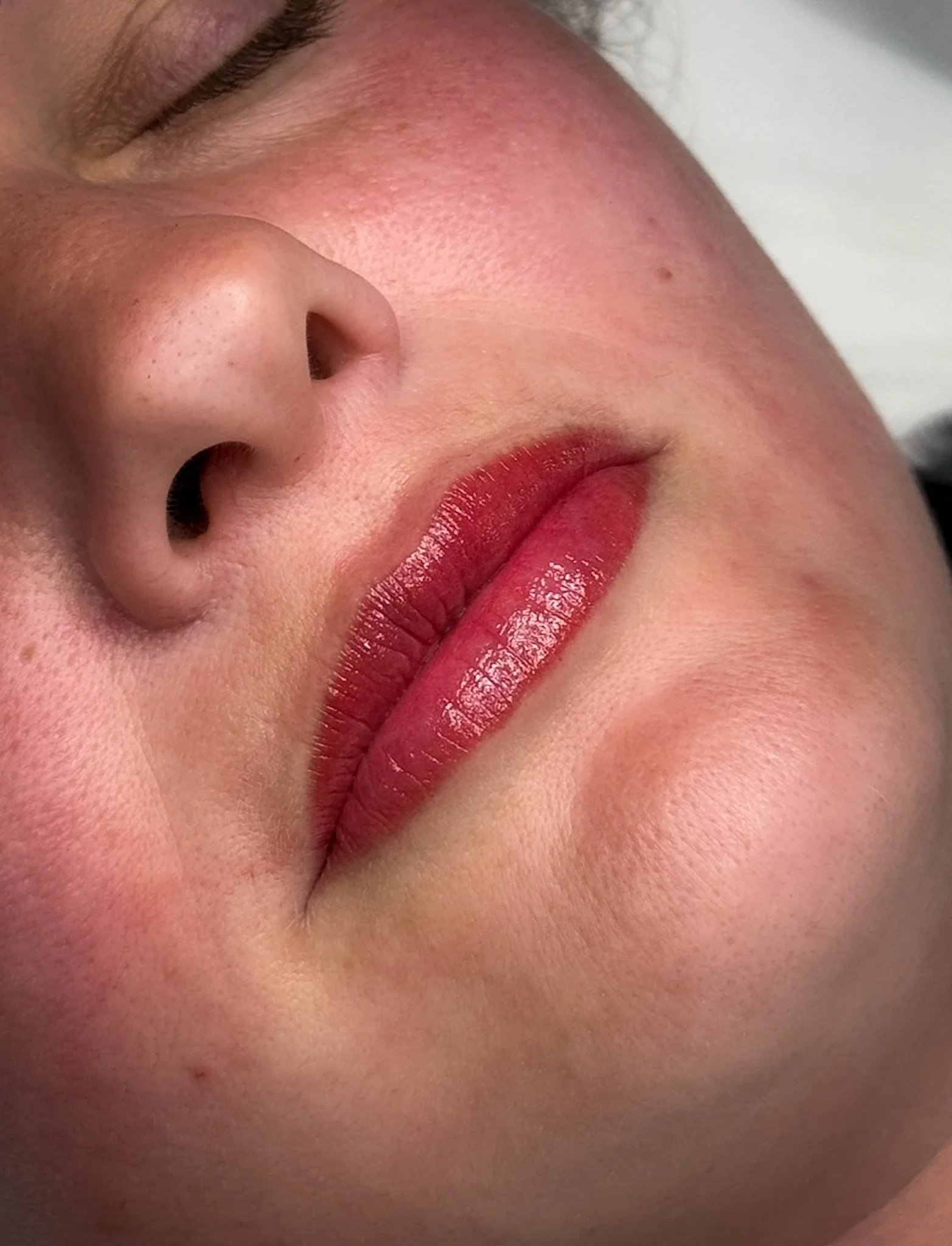 Close-up of a person's face focusing on the lips with glossy red lipstick and a nose with visible pores.
