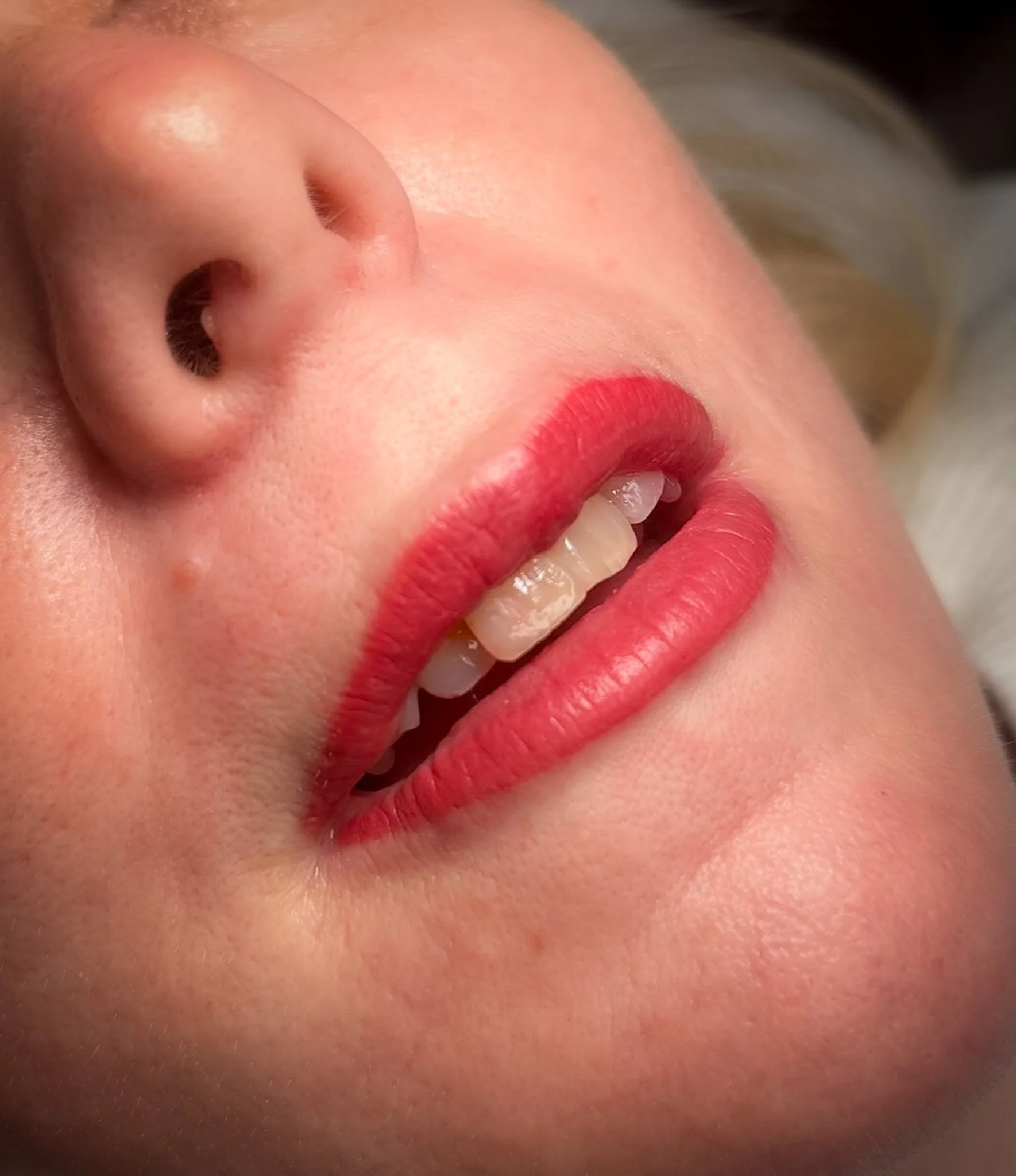 Close-up of a person's face showing the nose, lips painted with red lipstick, and teeth visible as they smile.