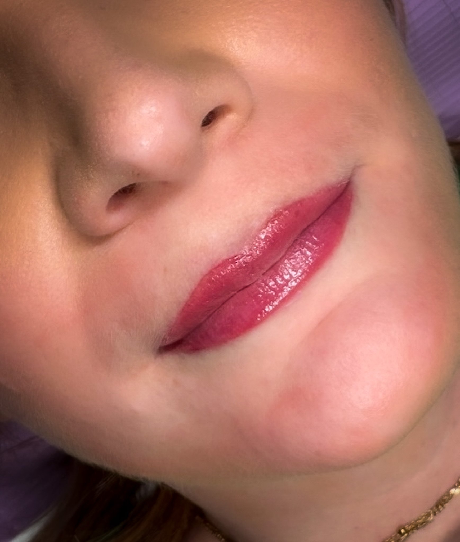 Close-up of a person's face showcasing a nose and lips with glossy lipstick.