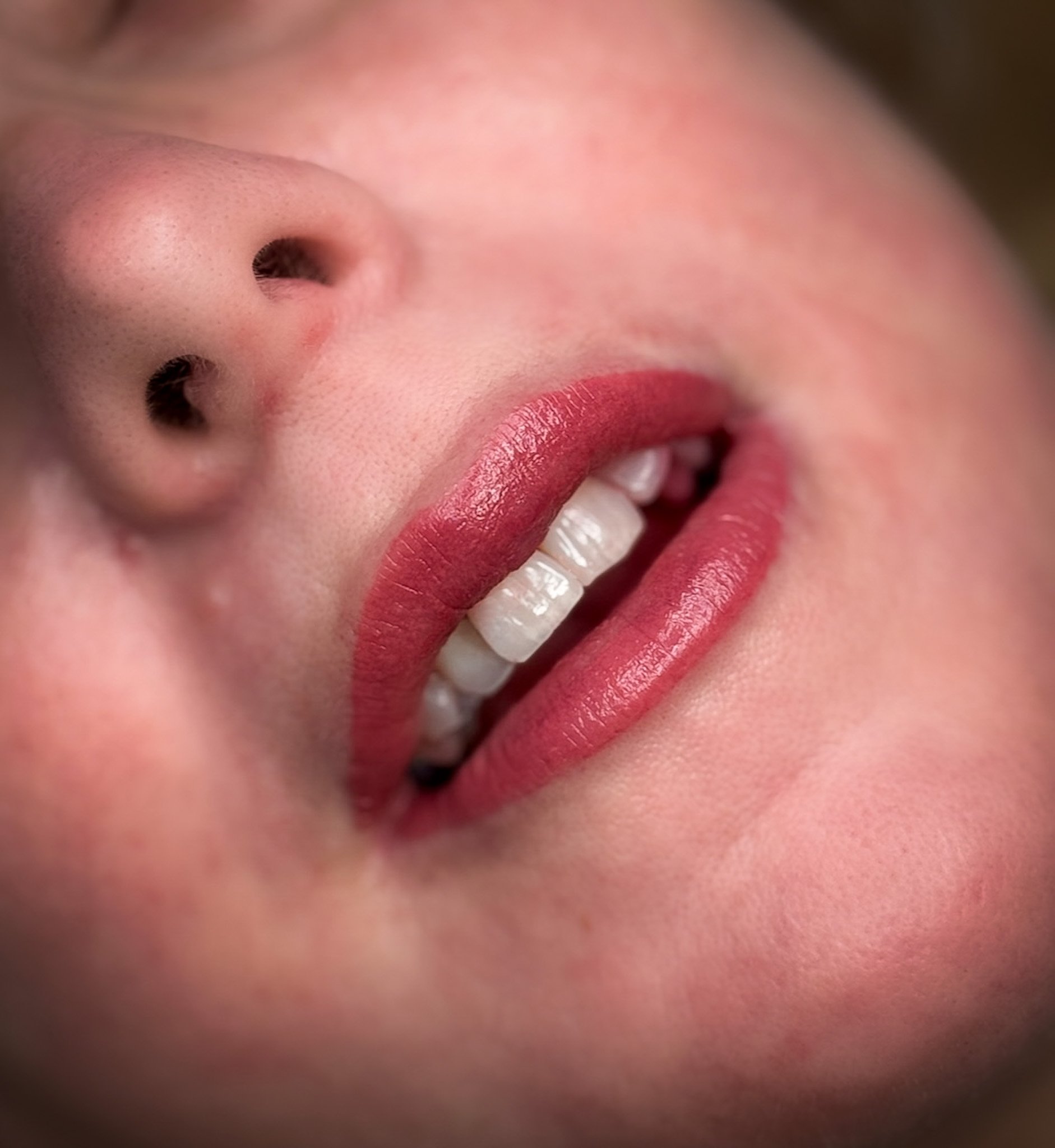 Close-up of a smiling person's face, showing lips with pink lipstick, nose, and teeth.