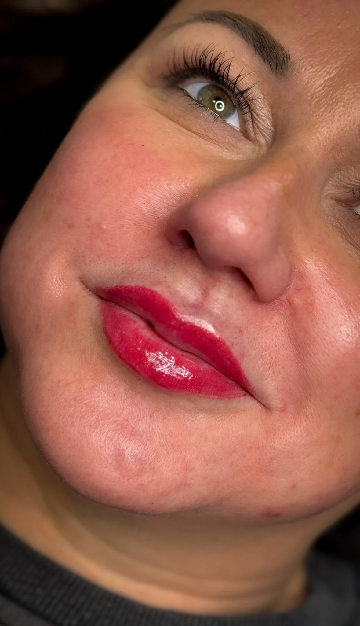 Close-up of a woman's face showing her eye, nose, and lips with red lipstick, with textured skin and some facial blemishes.