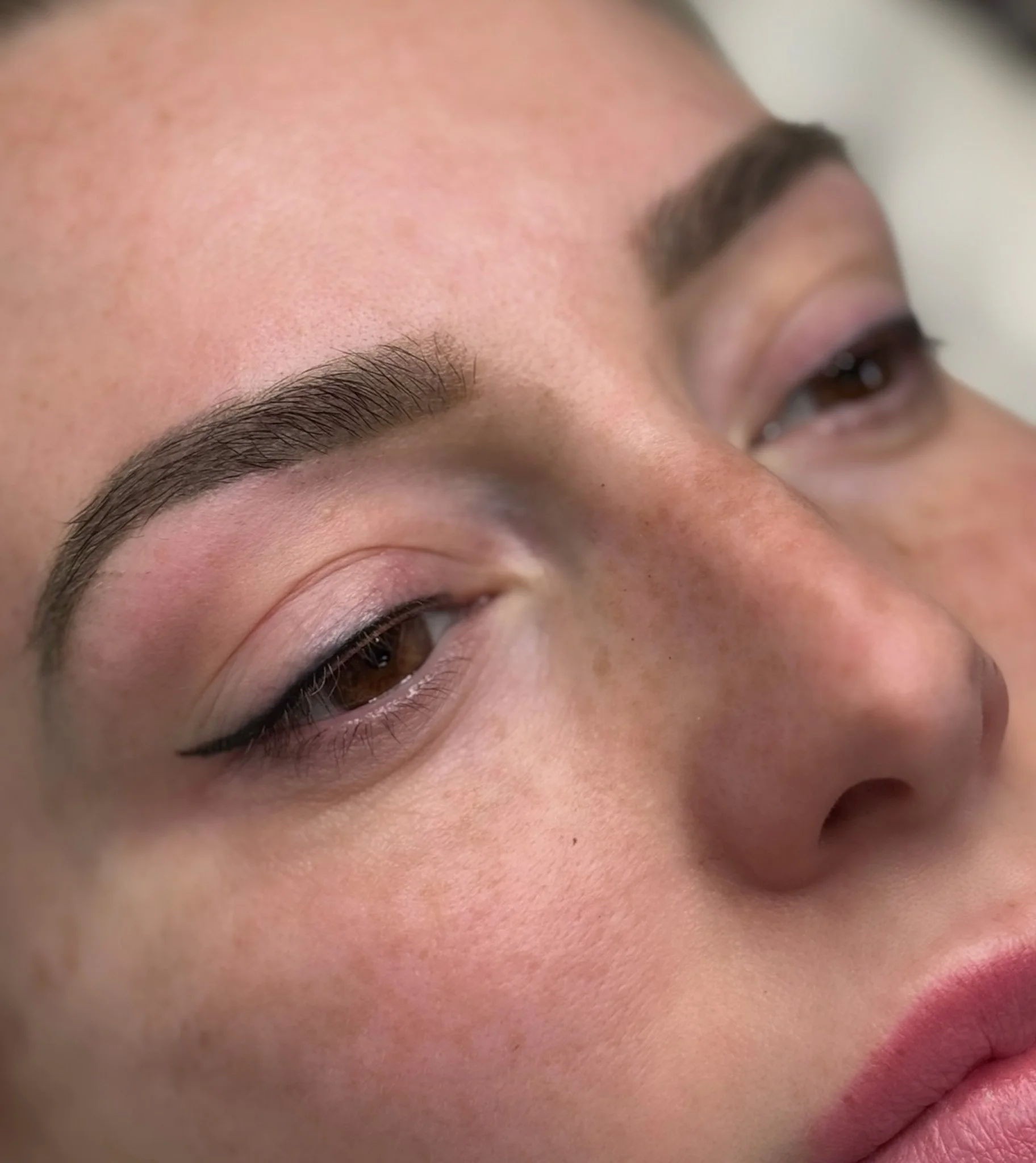 Close-up of a woman's face showing her eyebrows, eyes with makeup, and part of her nose and lips.