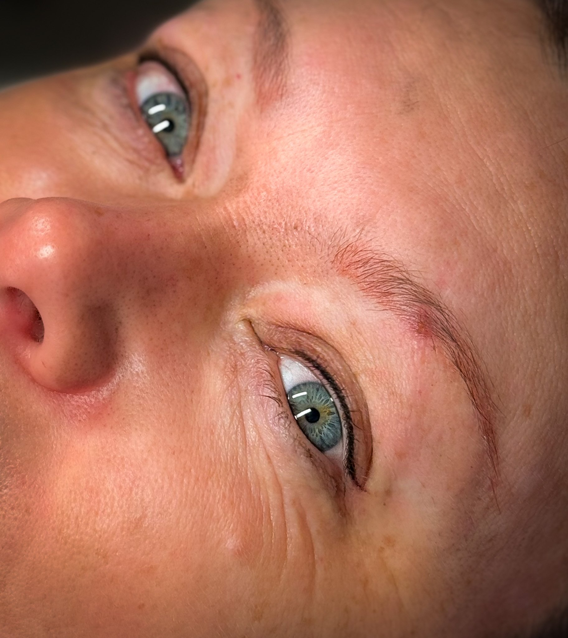 Close-up of a person's face lying down, showing their blue eyes, nose, and partially closed eyelids.