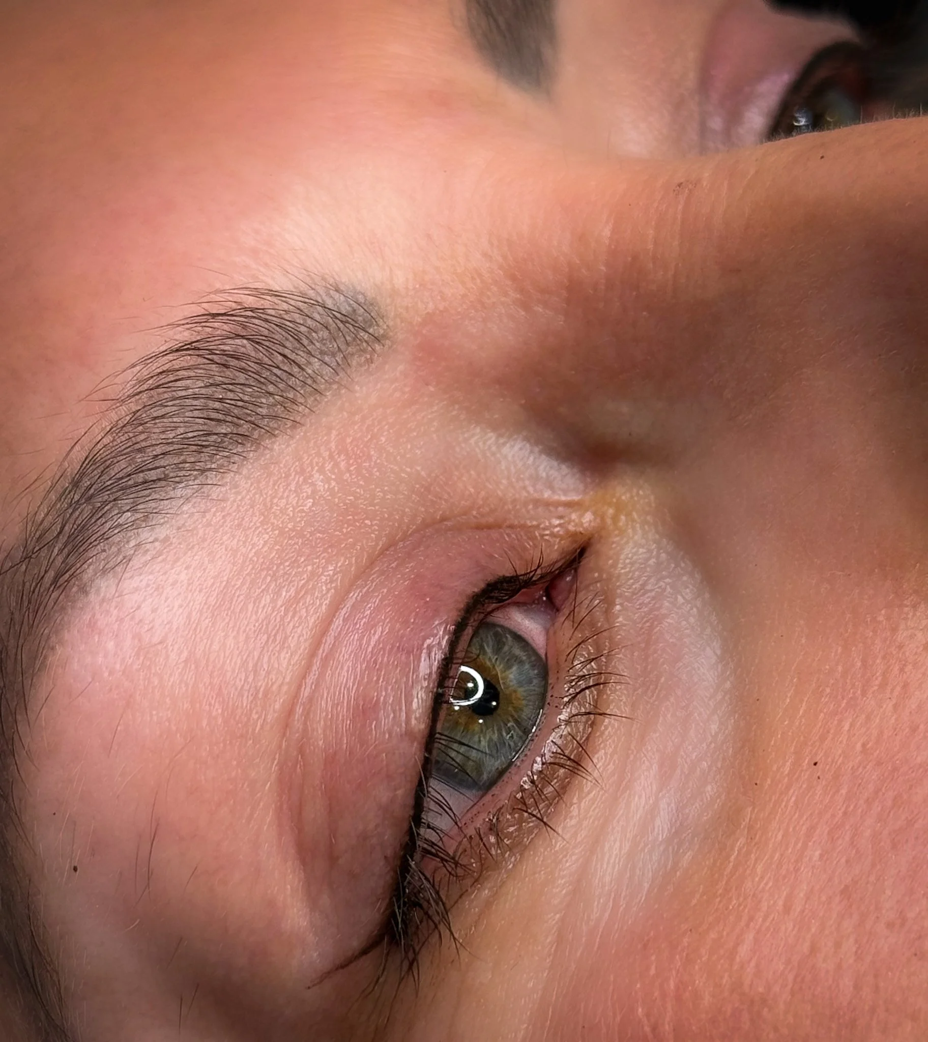 Close-up of a person's eye, showing detailed skin texture, eyebrow, and hazel eye with reflection of light.