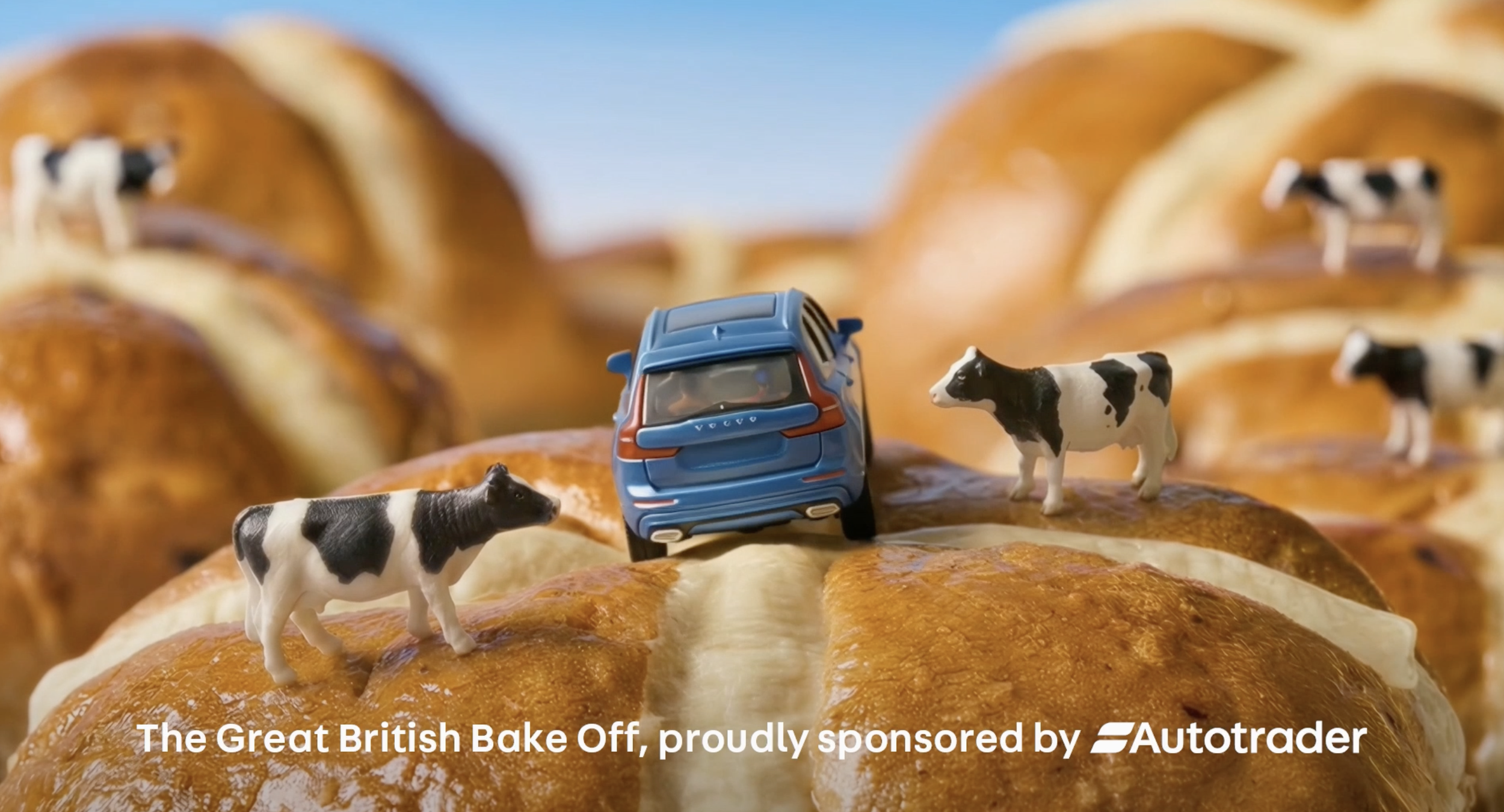 Miniature toy cows and a toy blue car on a baked pastry with melted cheese, with a background of baked pastries.