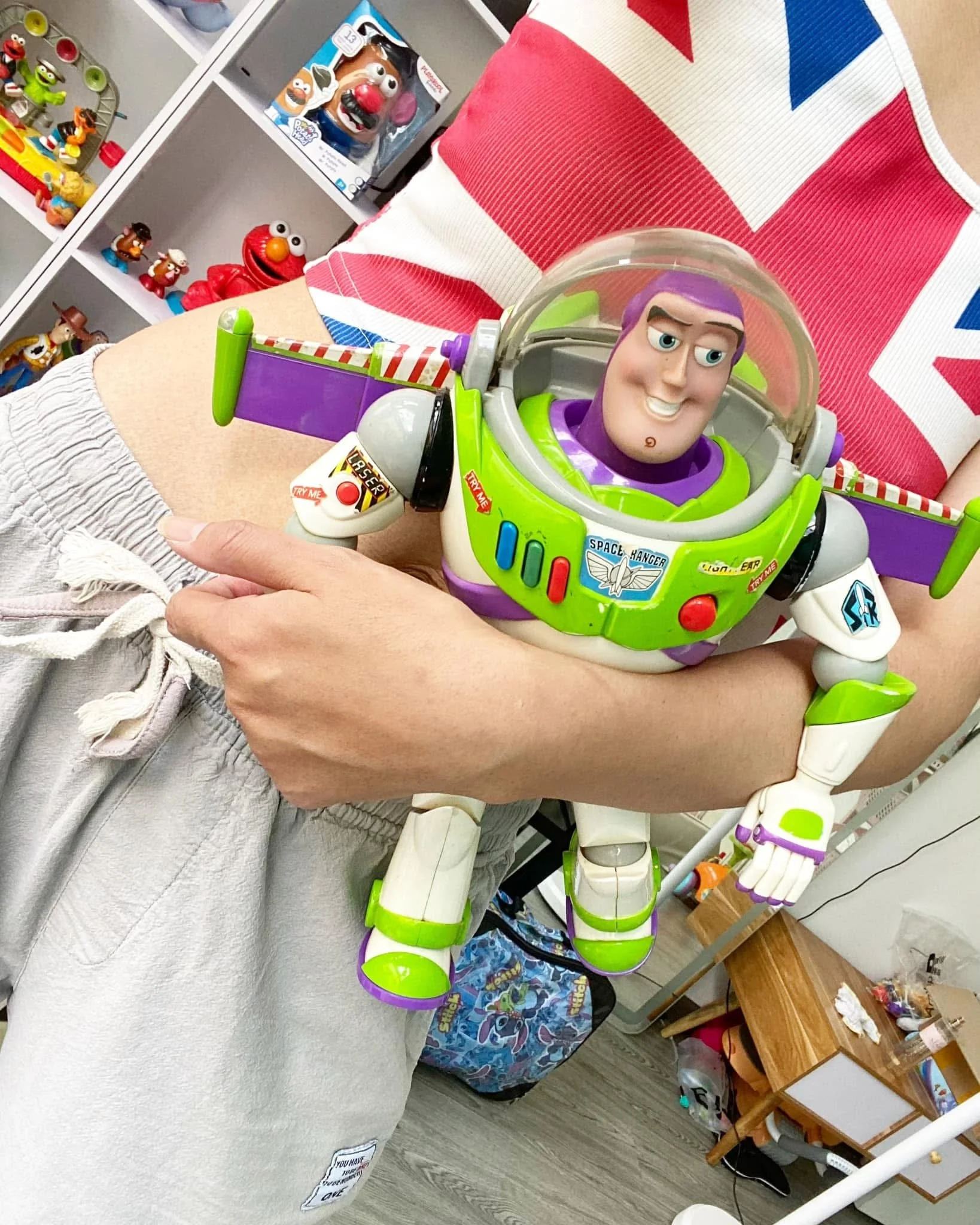 A person holding a Buzz Lightyear toy from Toy Story, with shelves of toys in the background.