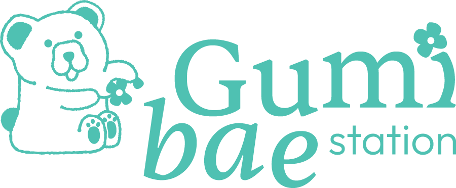 A logo with a drawing of a bear holding a flower, next to the text "Gumi Ba Station" with a small flower over the "i" in "Gumi".