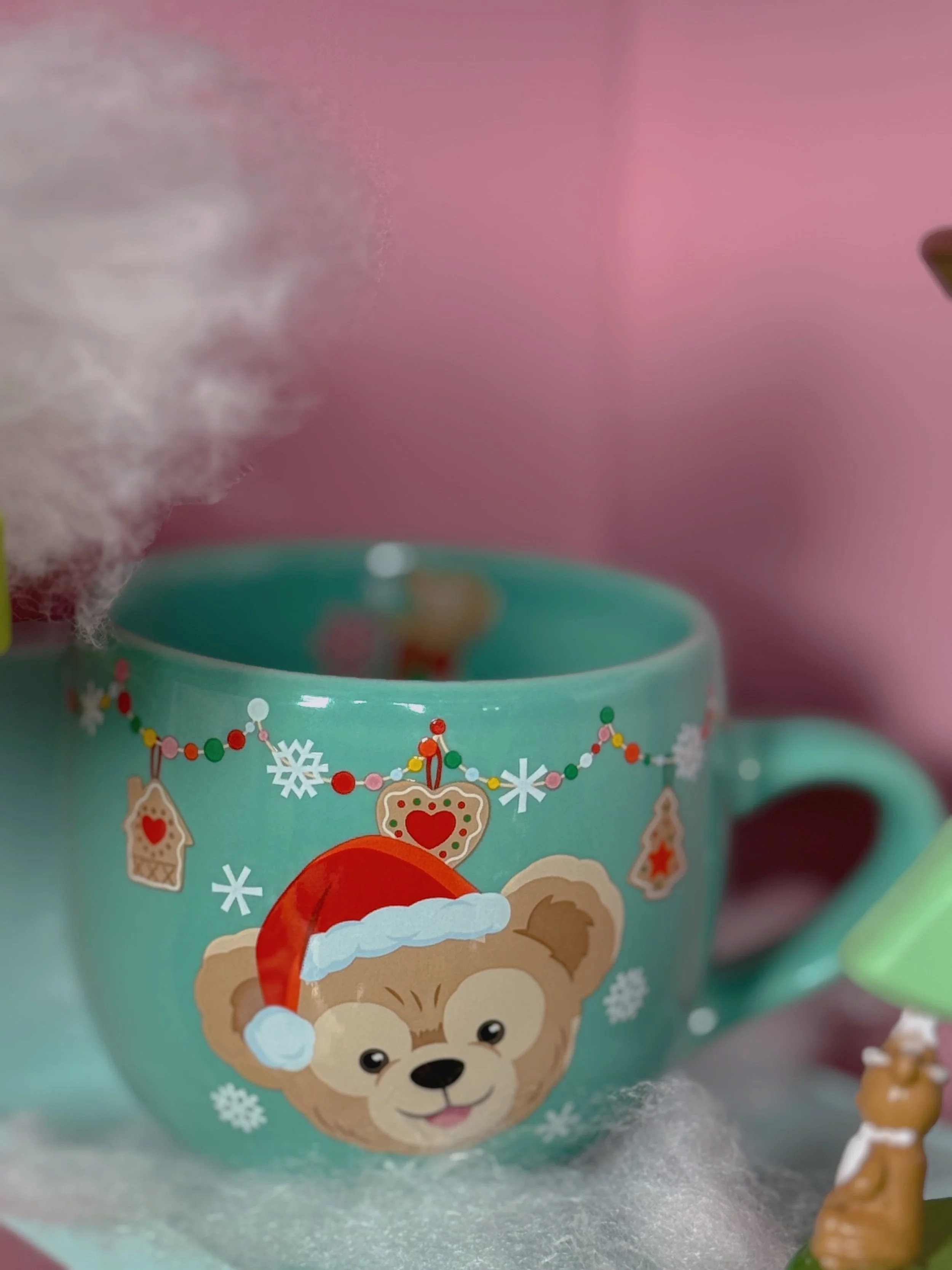 Mint green Christmas mug with a cartoon bear wearing a Santa hat, decorated with holiday ornaments and snowflakes, filled with hot beverage and steam rising.