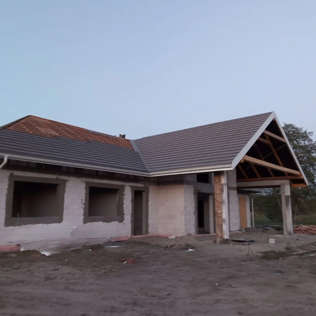 Budowa domu jednorodzinnego z więźbą dachową i pokryciem ceramicznym – etap krycia dachu dachówką.