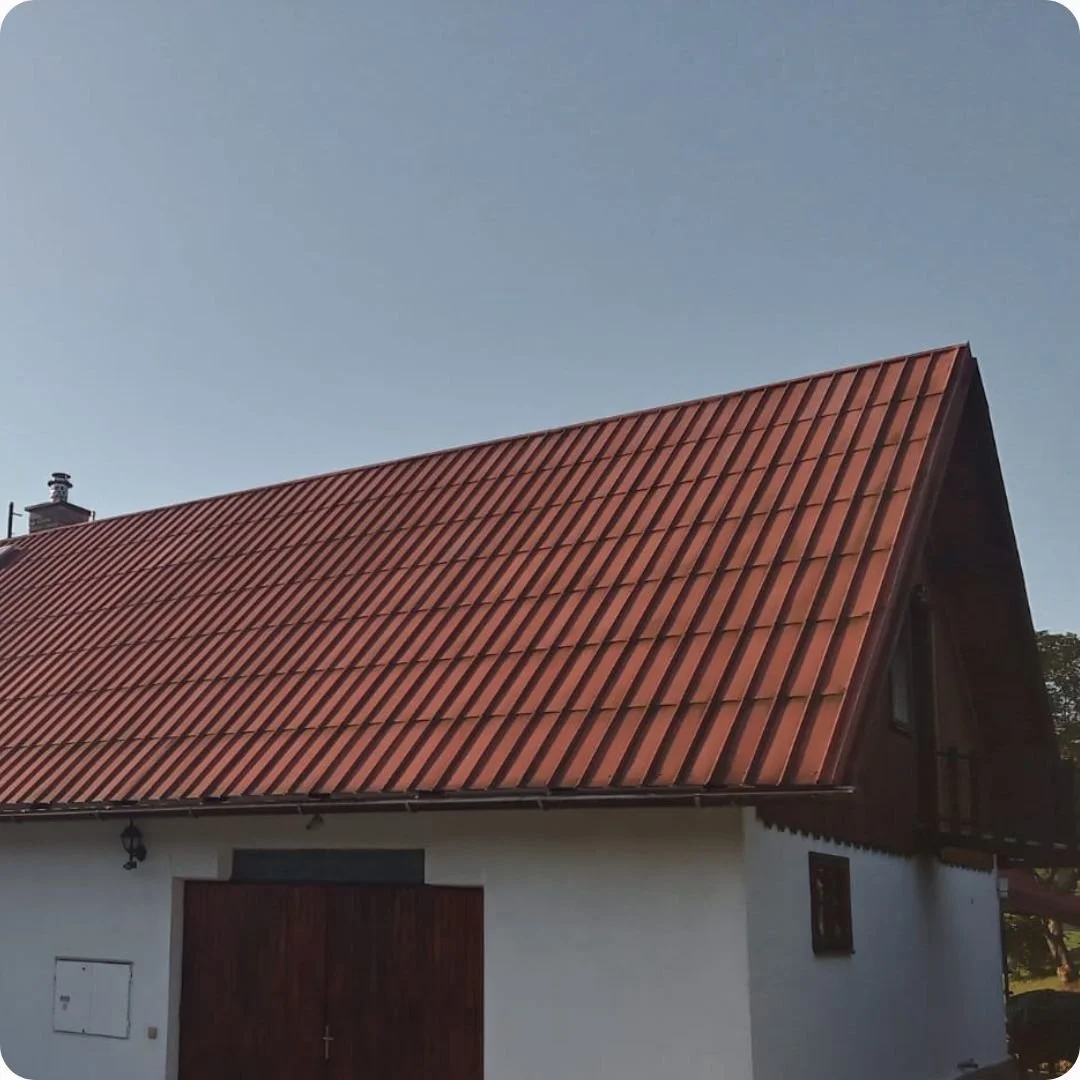 Czerwony dach z paneli na rąbek stojący na białym budynku z dużym spadkiem połaci.