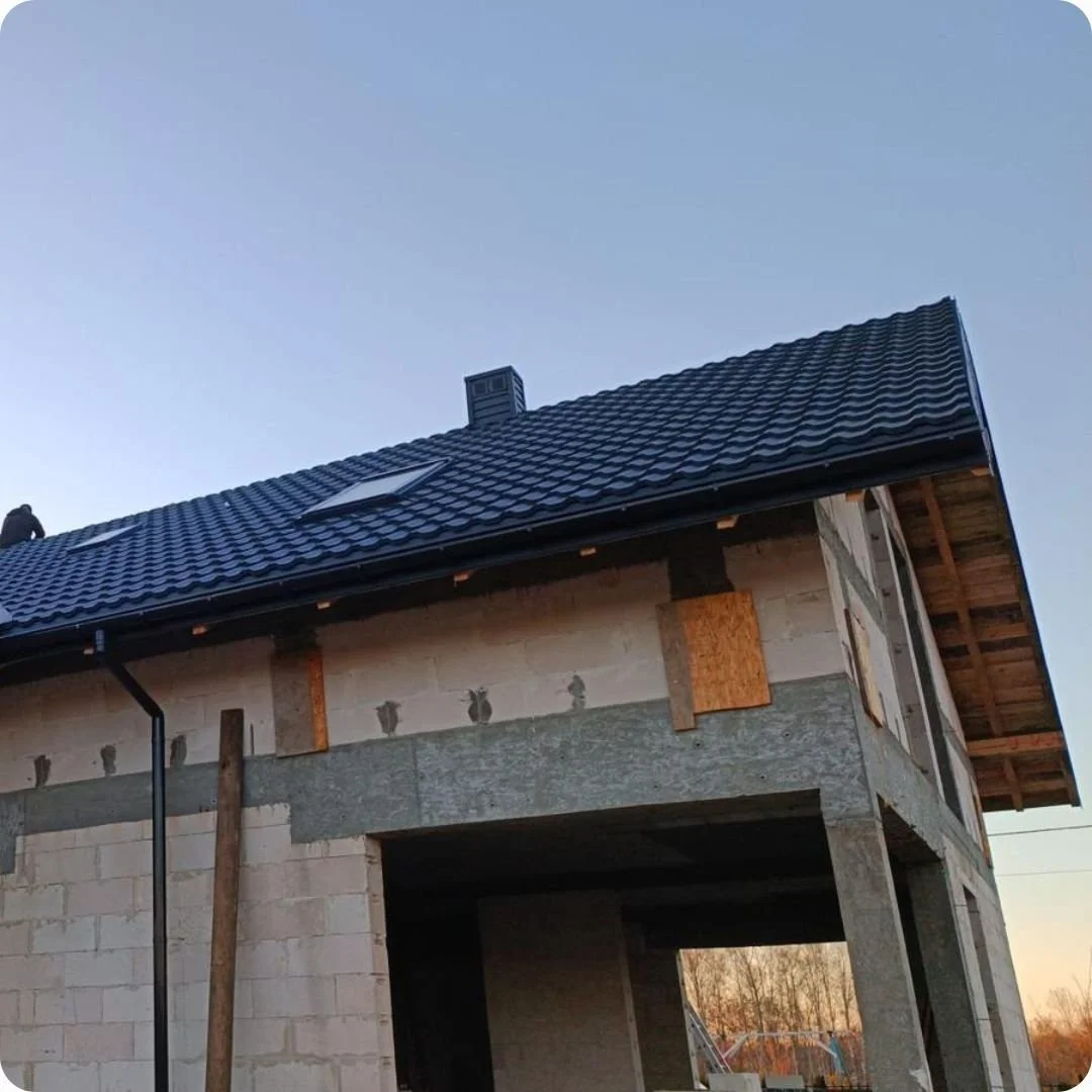 Czarny dach z blachodachówki z oknem dachowym i rynną w budowie.