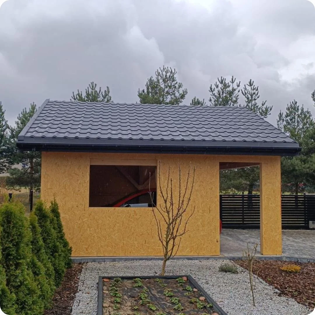 Garaż z dachem z blachodachówki i elewacją z płyty OSB, w tle ogród.