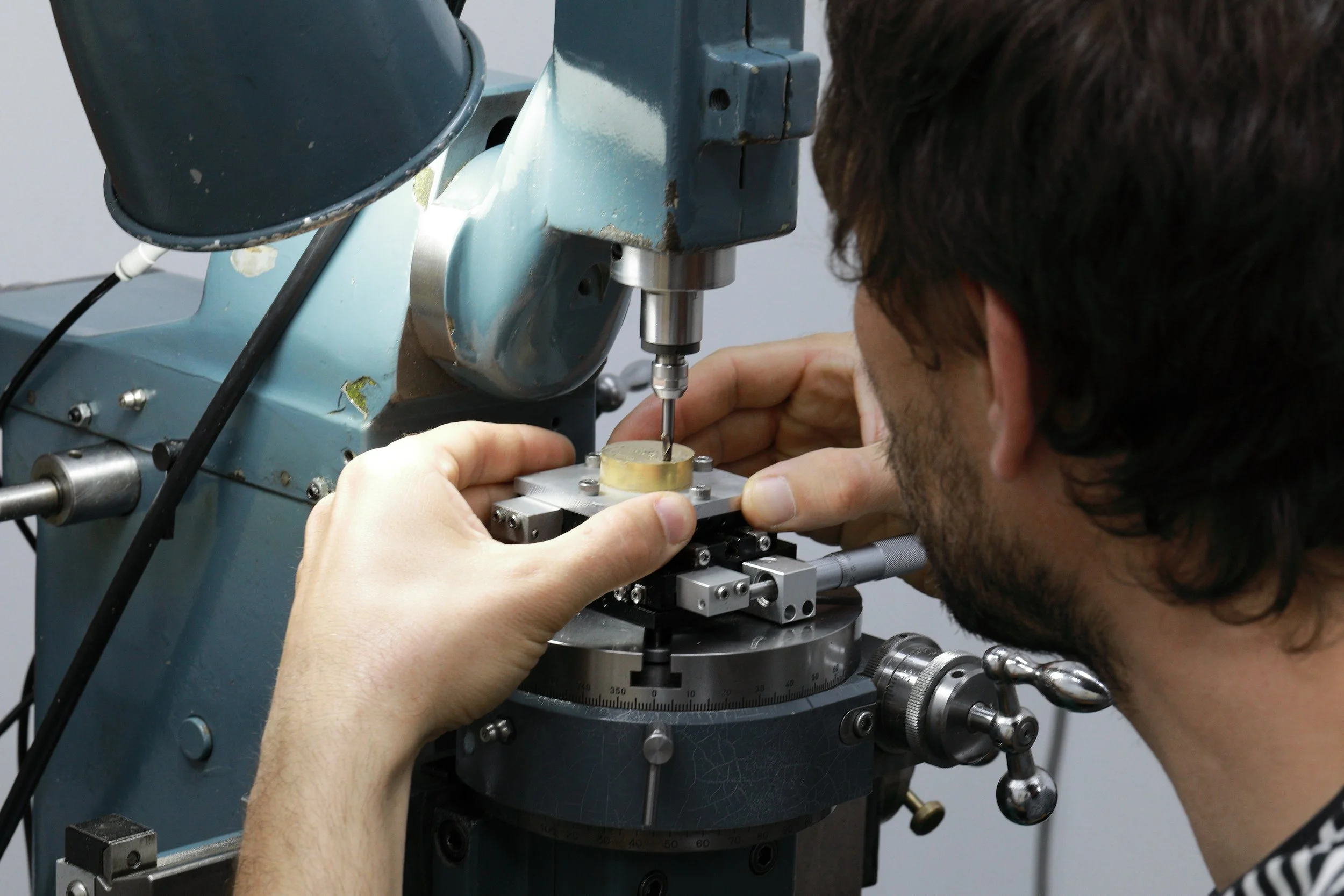 A person operating a precision machine while working on a small metallic component.