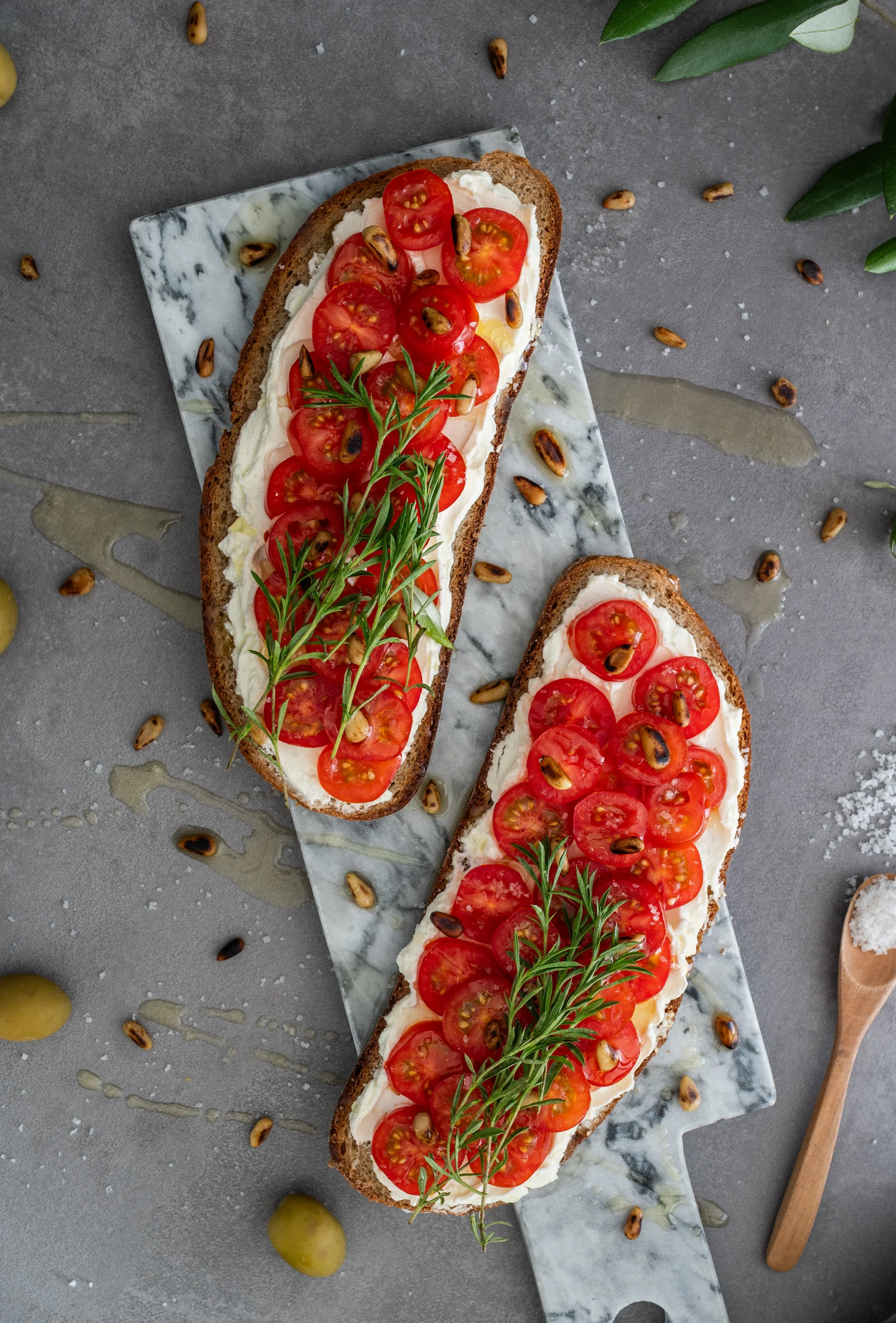 Zweibrote mit Frischkäse, halbierten Cherrytomaten, Thymian und gerösteten Sonnenblumenkernen, serviert auf einem Marmorbrett