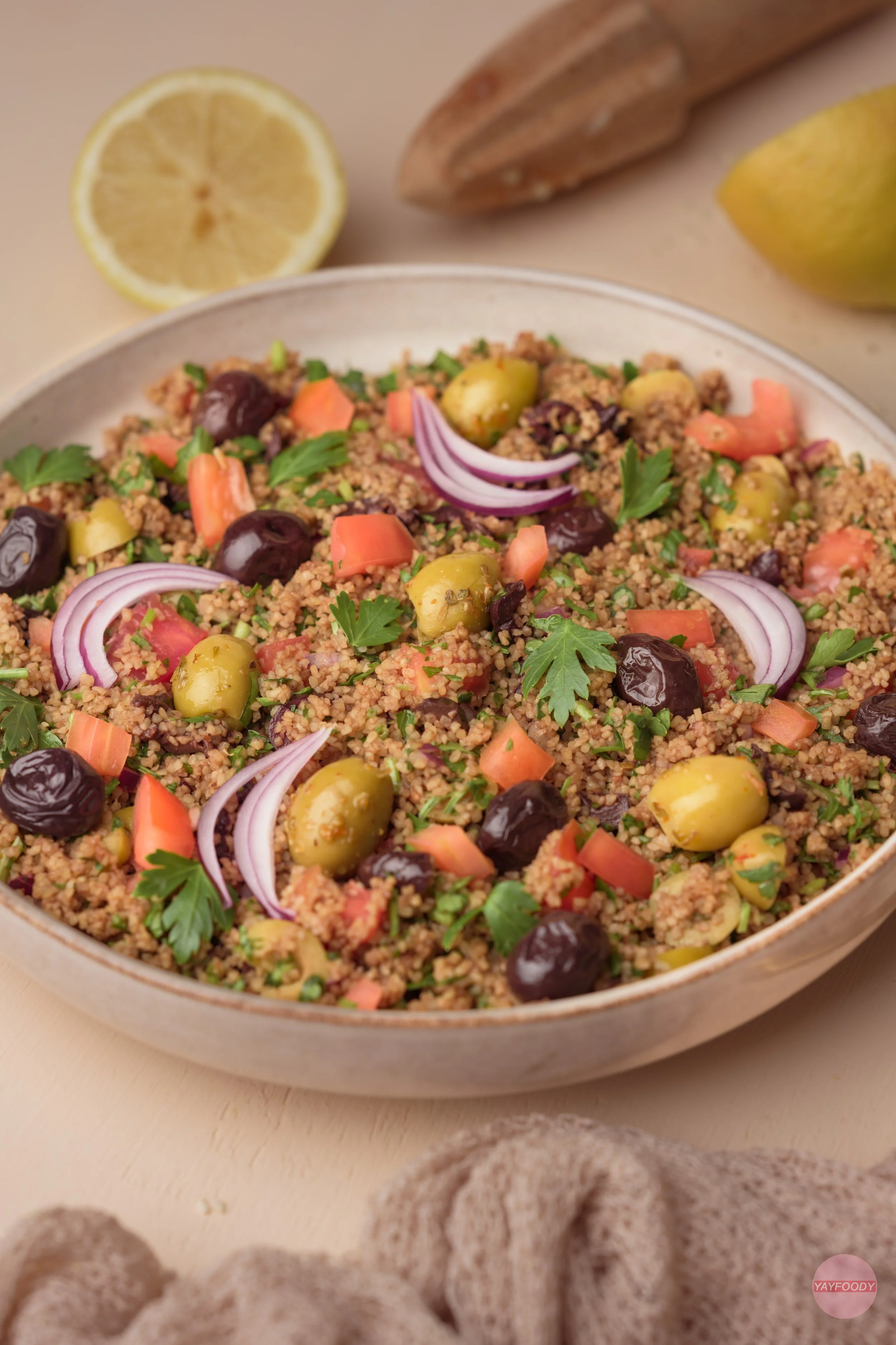 Bunter Bulgursalat mit Oliven, roten Zwiebeln, Tomaten und frischen Kräutern in einer Schüssel.