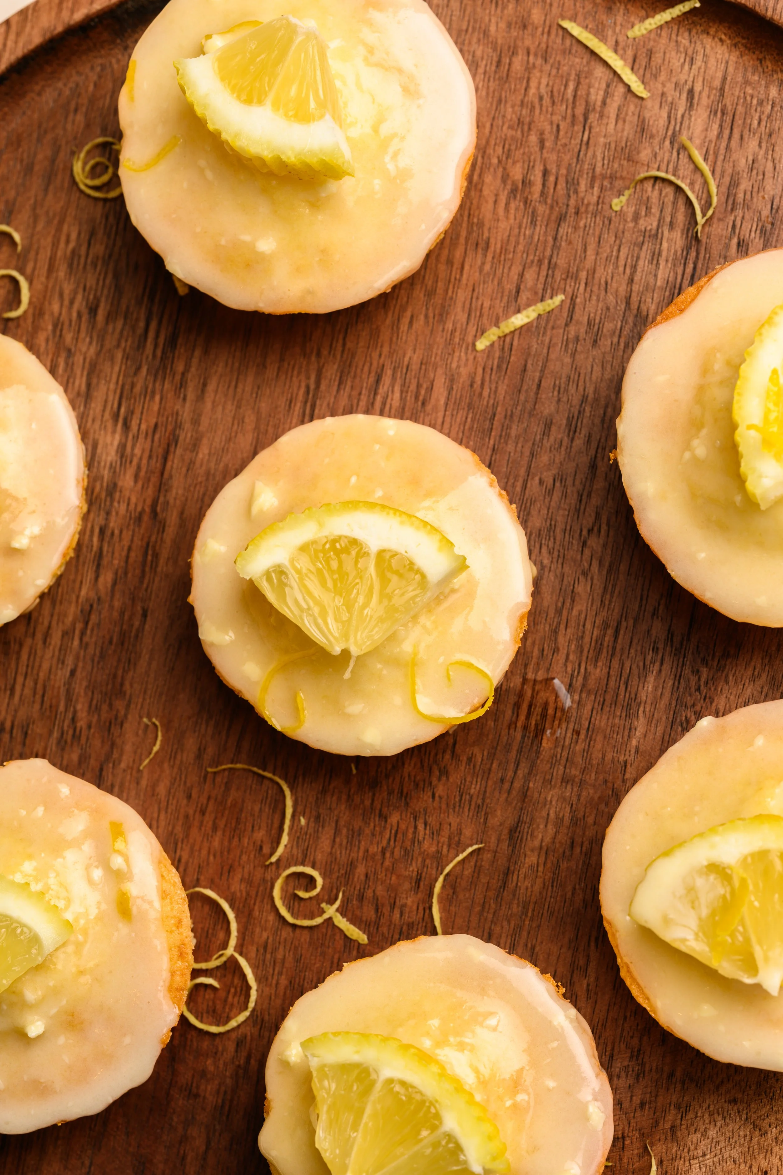 Zitronenkuchen Muffins mit Zitronenscheiben und Zitronenzesten auf einem Holzbrett.