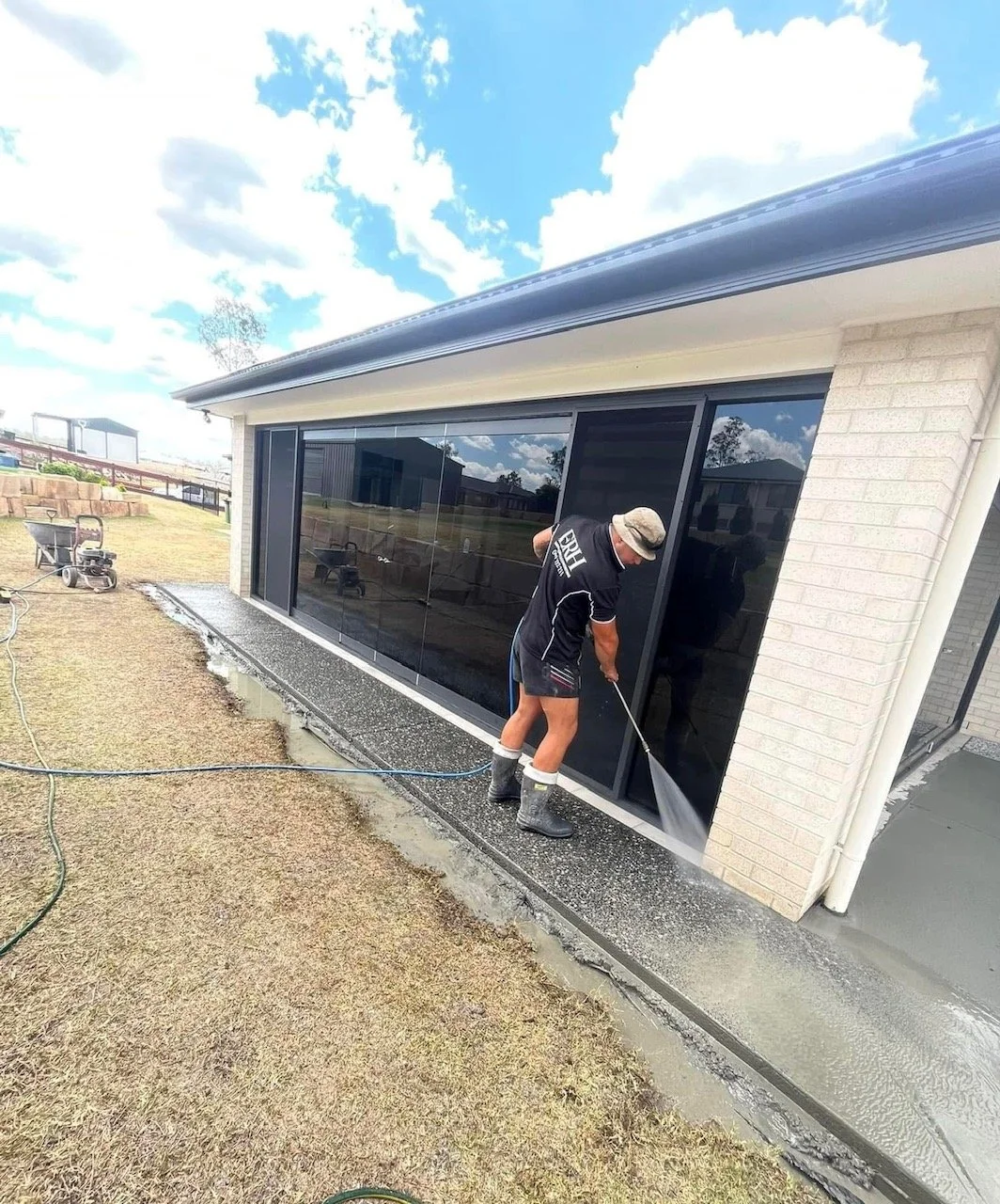 Person cleaning the glass sliding door of a house with a power washer on a sunny day.
