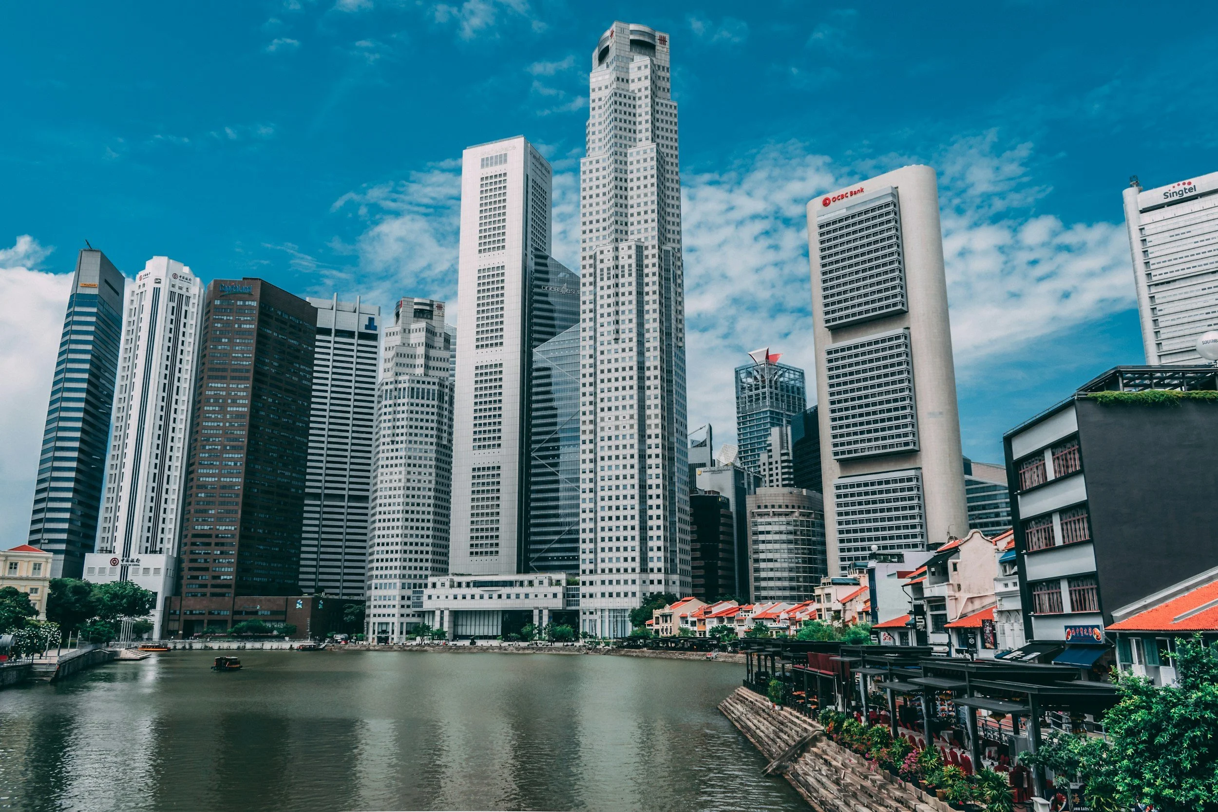 Singapore skyline with tall modern skyscrapers along a river under a partly cloudy sky.