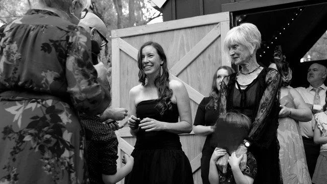 Proud mother of the bride with white hair watches her daughter put the ring on her new husband whilst laughing