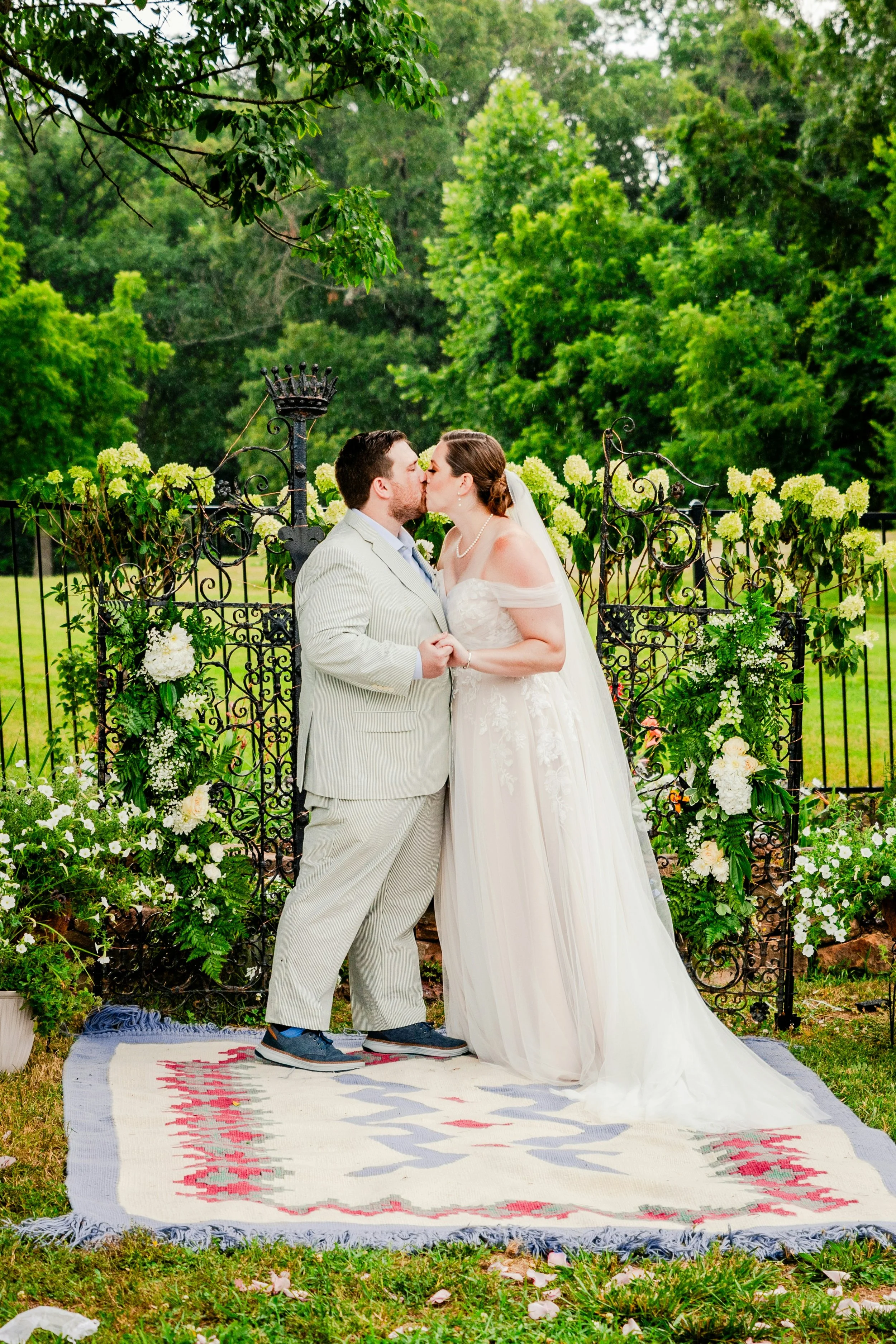 A bride and groom get married on a picnic blanket surrounded by green trees.