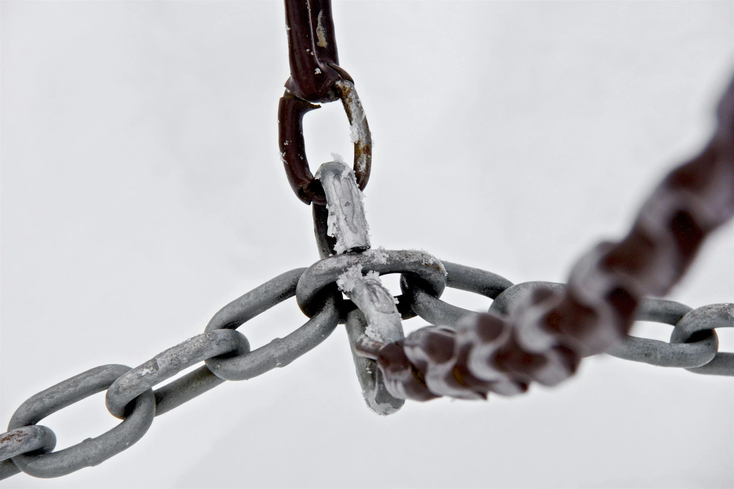 Close-up of rusted chain links connected and covered with ice, with snow in the background.