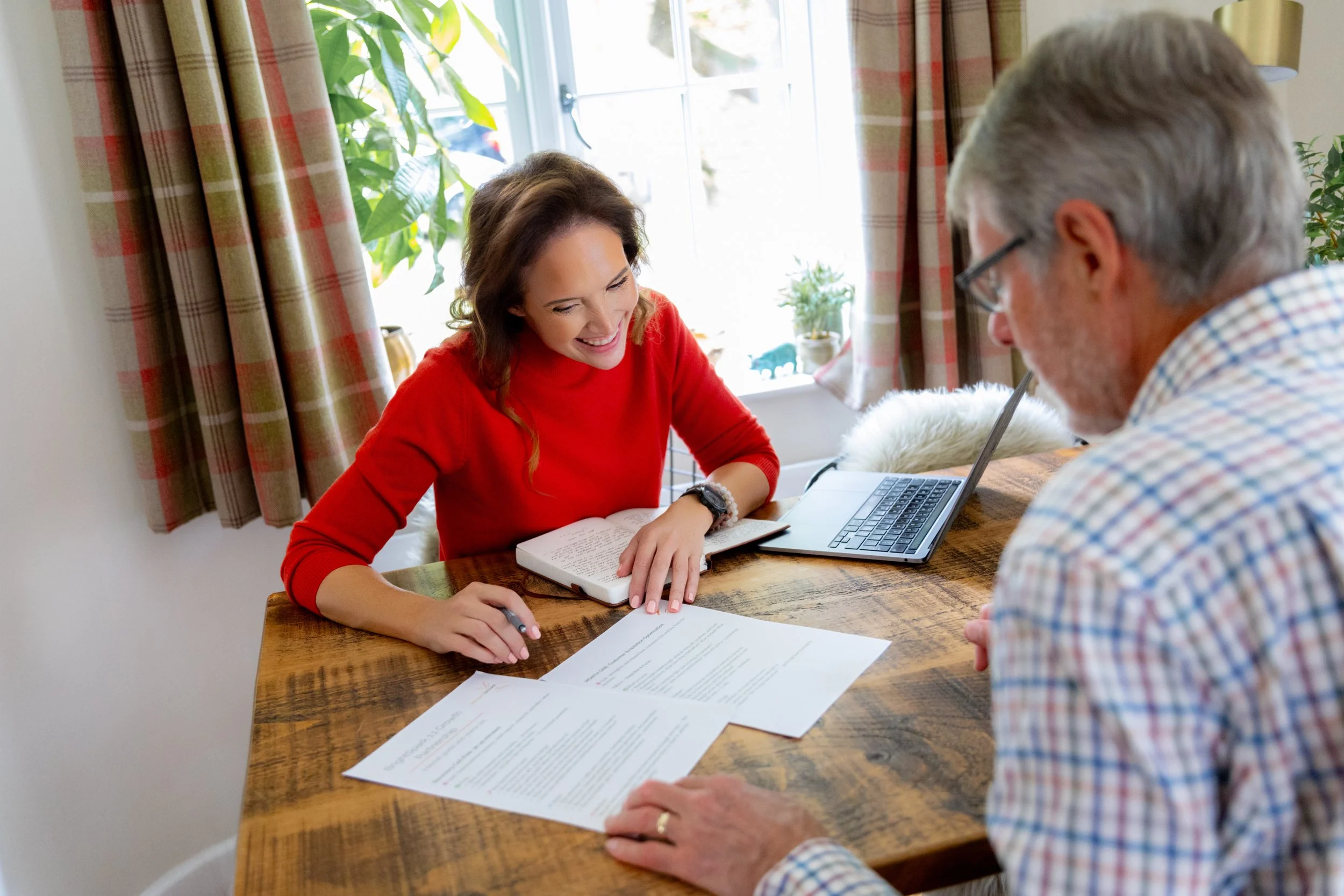 Sam at a desk working with an older, male client.  Both are looking at the paperwork between them.
