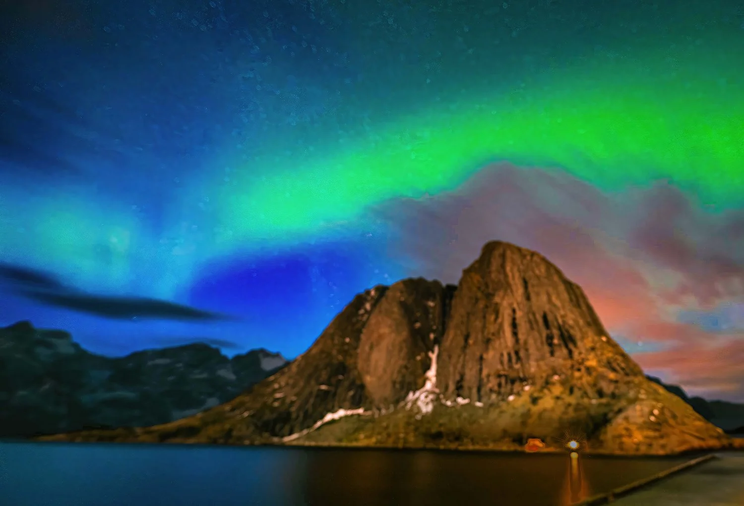 Nighttime scene of a mountain with the Northern Lights (aurora borealis) in green and blue colors across the sky, with some clouds and stars visible.
