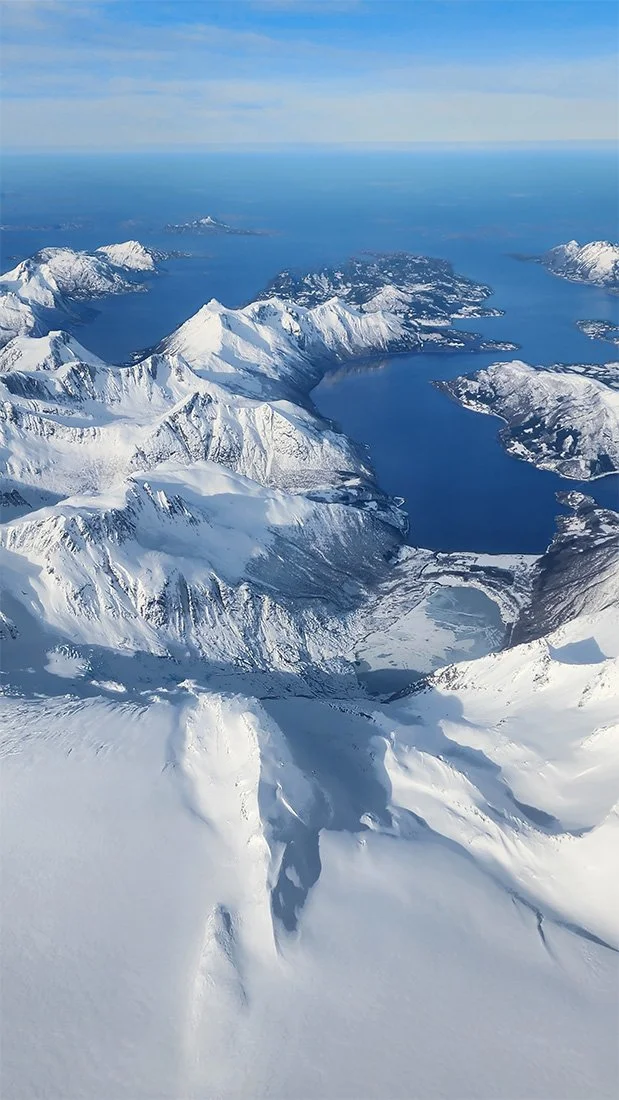 Aerial view of snow-covered mountains and deep blue water bodies in a polar region.