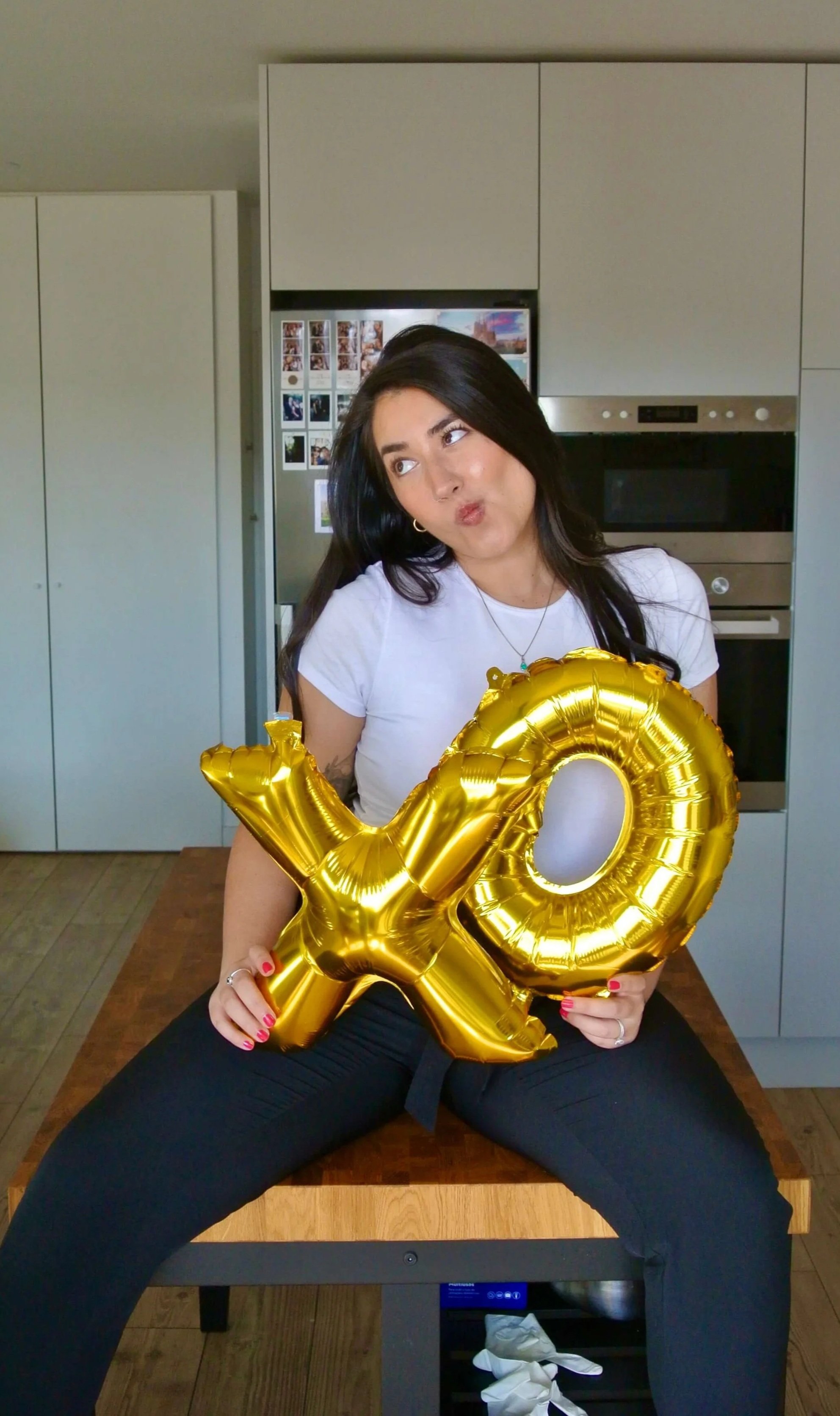 Ariel De La Mora holding XO balloons while sitting on a kitchen island