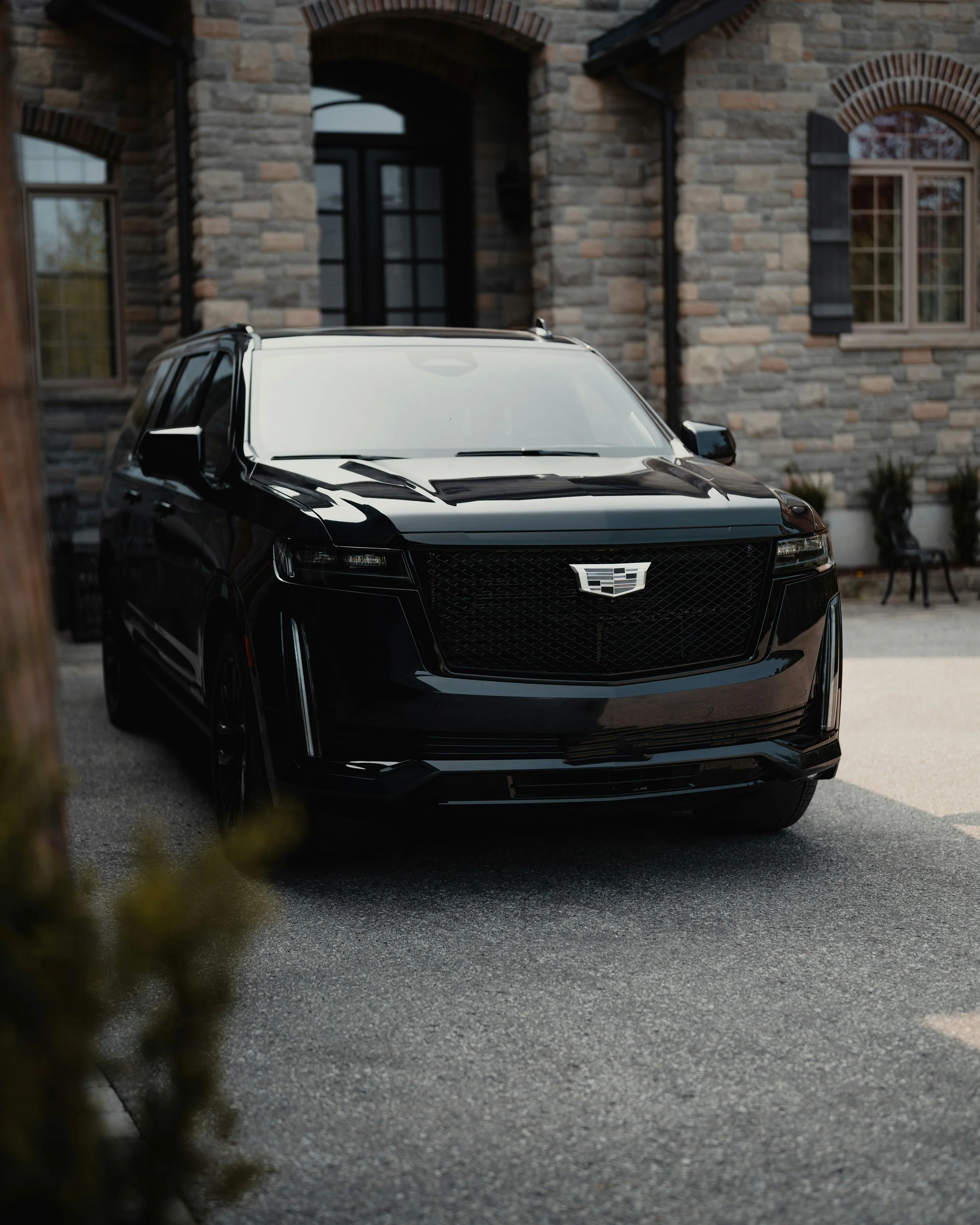 Black Cadillac SUV parked in front of a house with stone exterior and multiple windows.