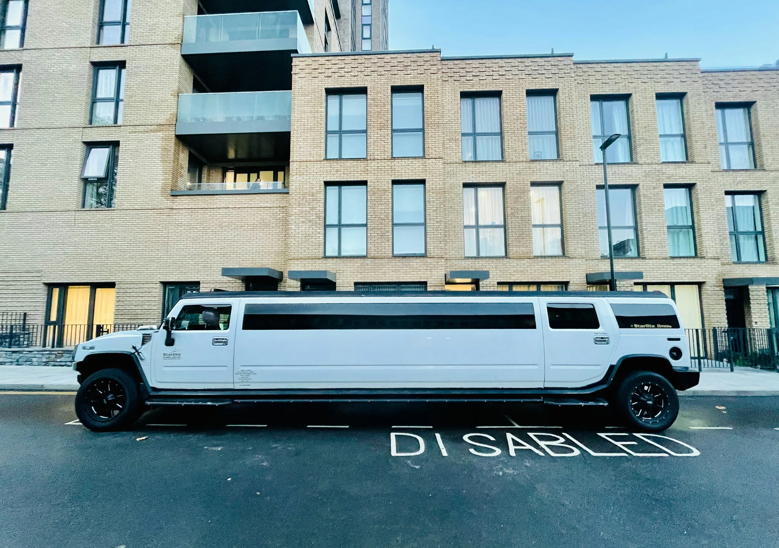 A white stretch limousine parked on a Dallas city street in front of a modern brick apartment building.
