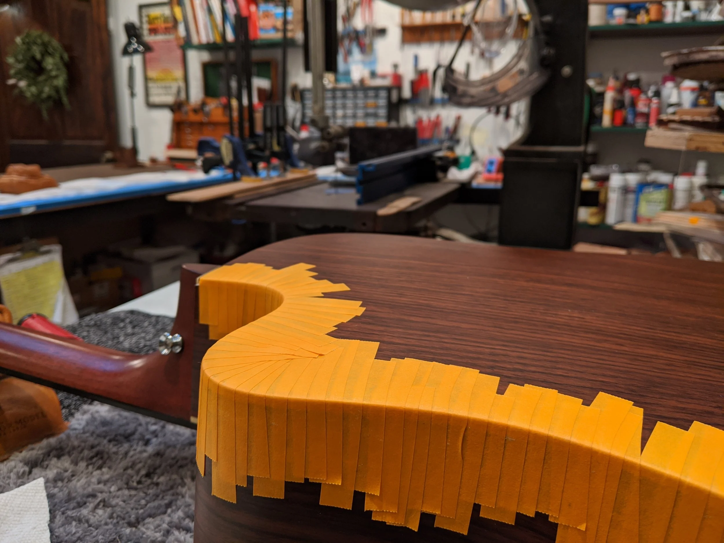A woodworking workshop with a partially assembled wooden piece on a workbench, surrounded by tools and supplies.