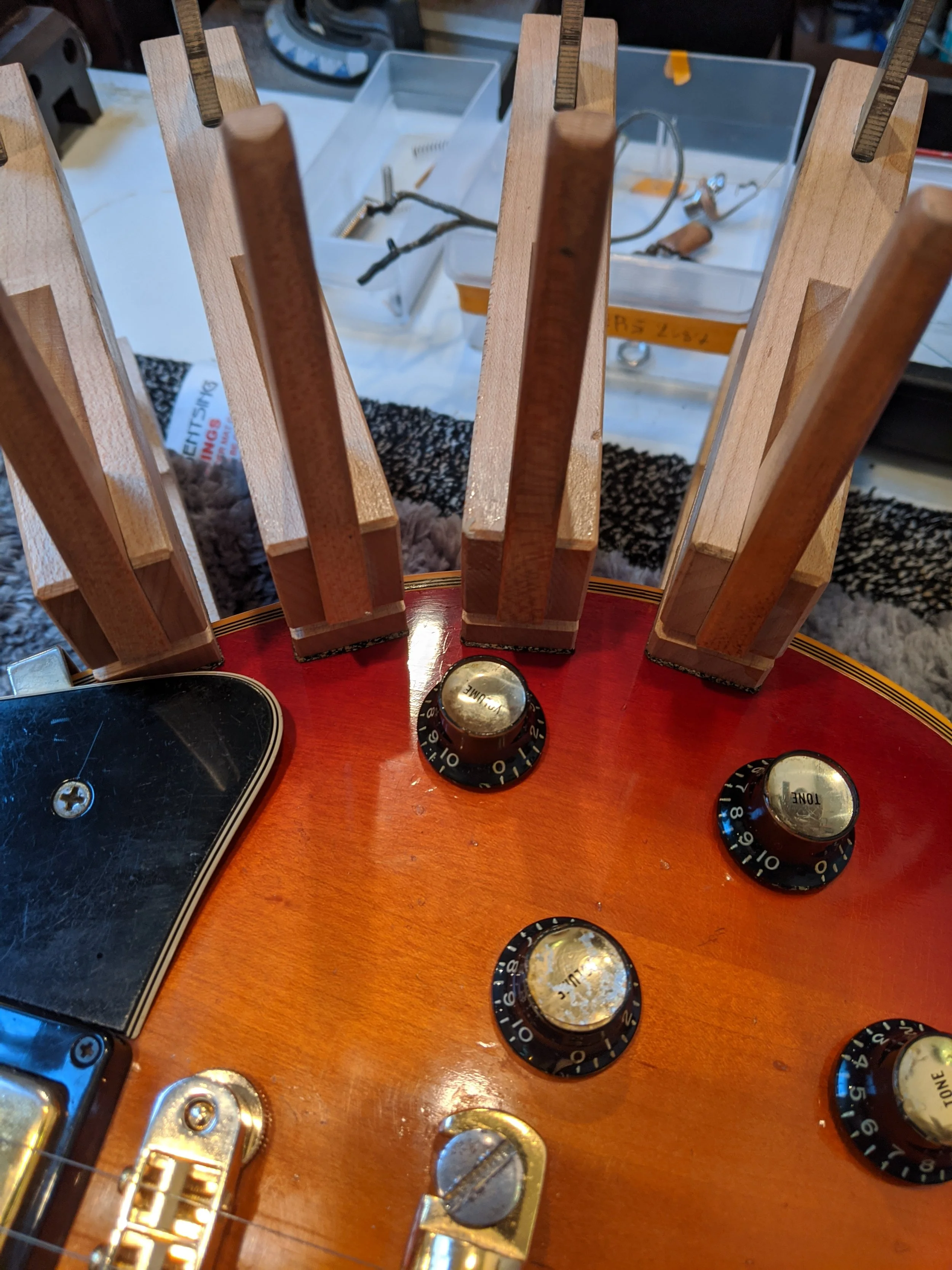 Close-up of a guitar's control knobs and wooden tuning pegs in a workshop setting.