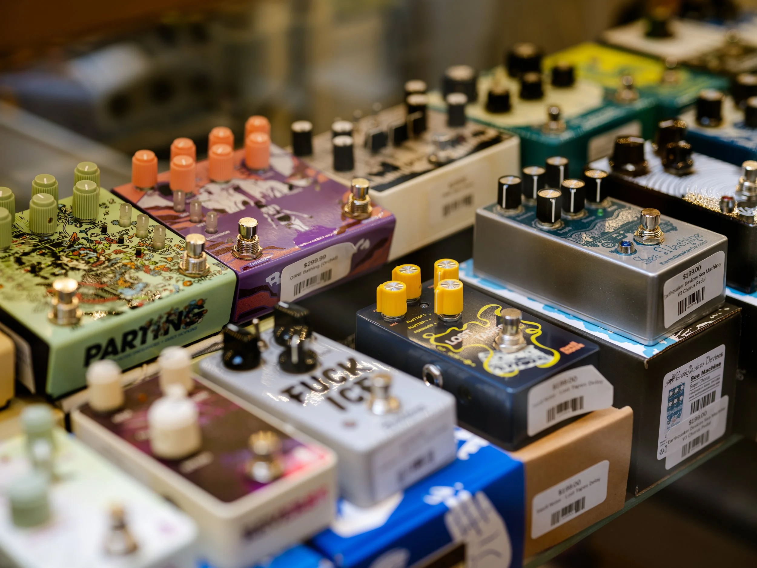 Close-up of multiple guitar effect pedals arranged on a shelf, featuring colorful and labeled controls.