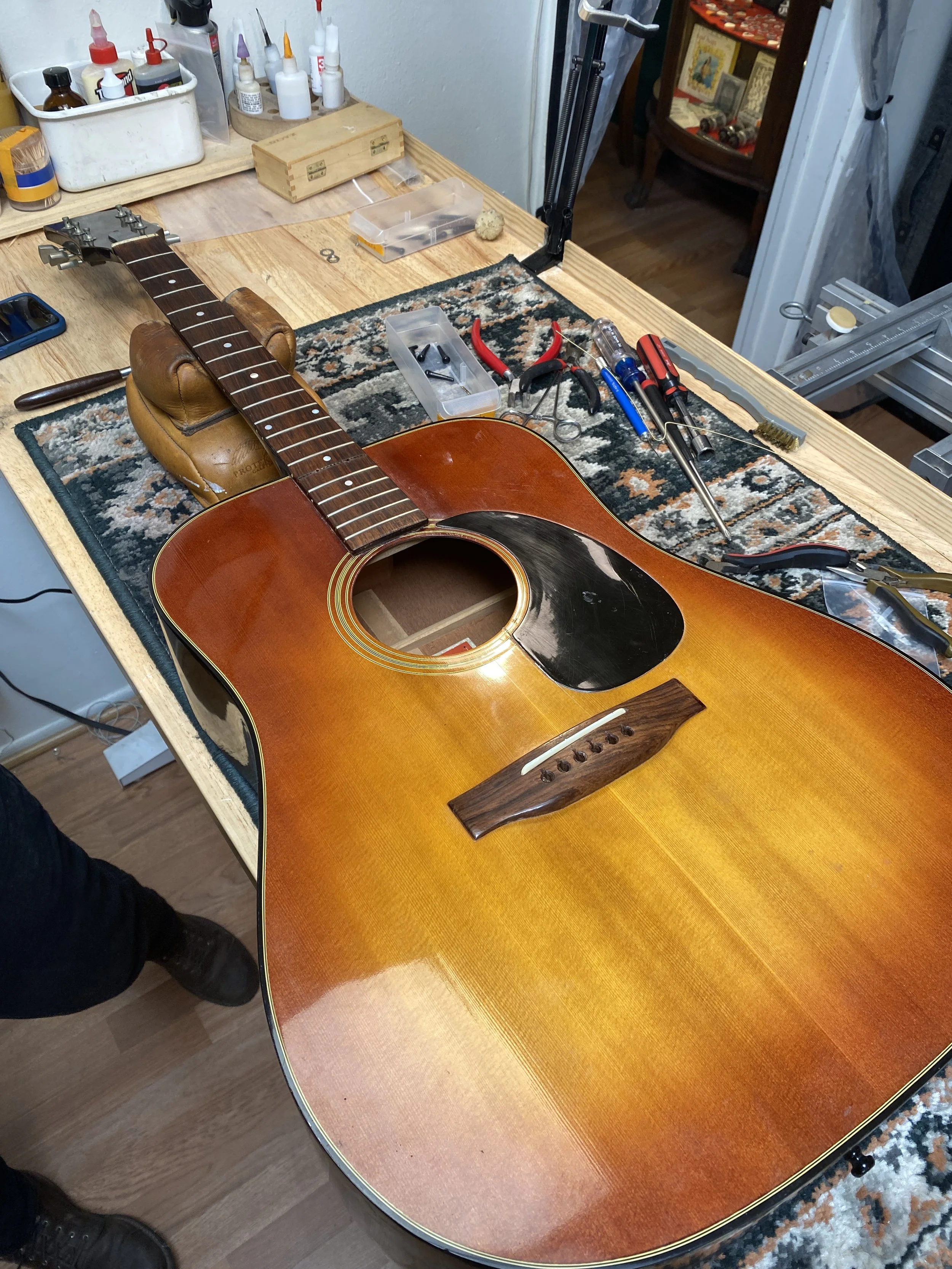 Disassembled acoustic guitar on a workbench surrounded by repair tools and supplies.