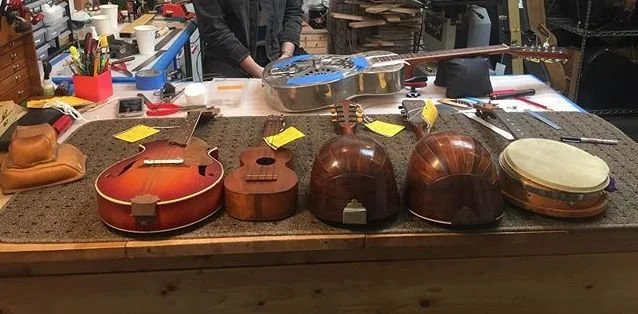Several guitars and a tambourine on a workshop table.
