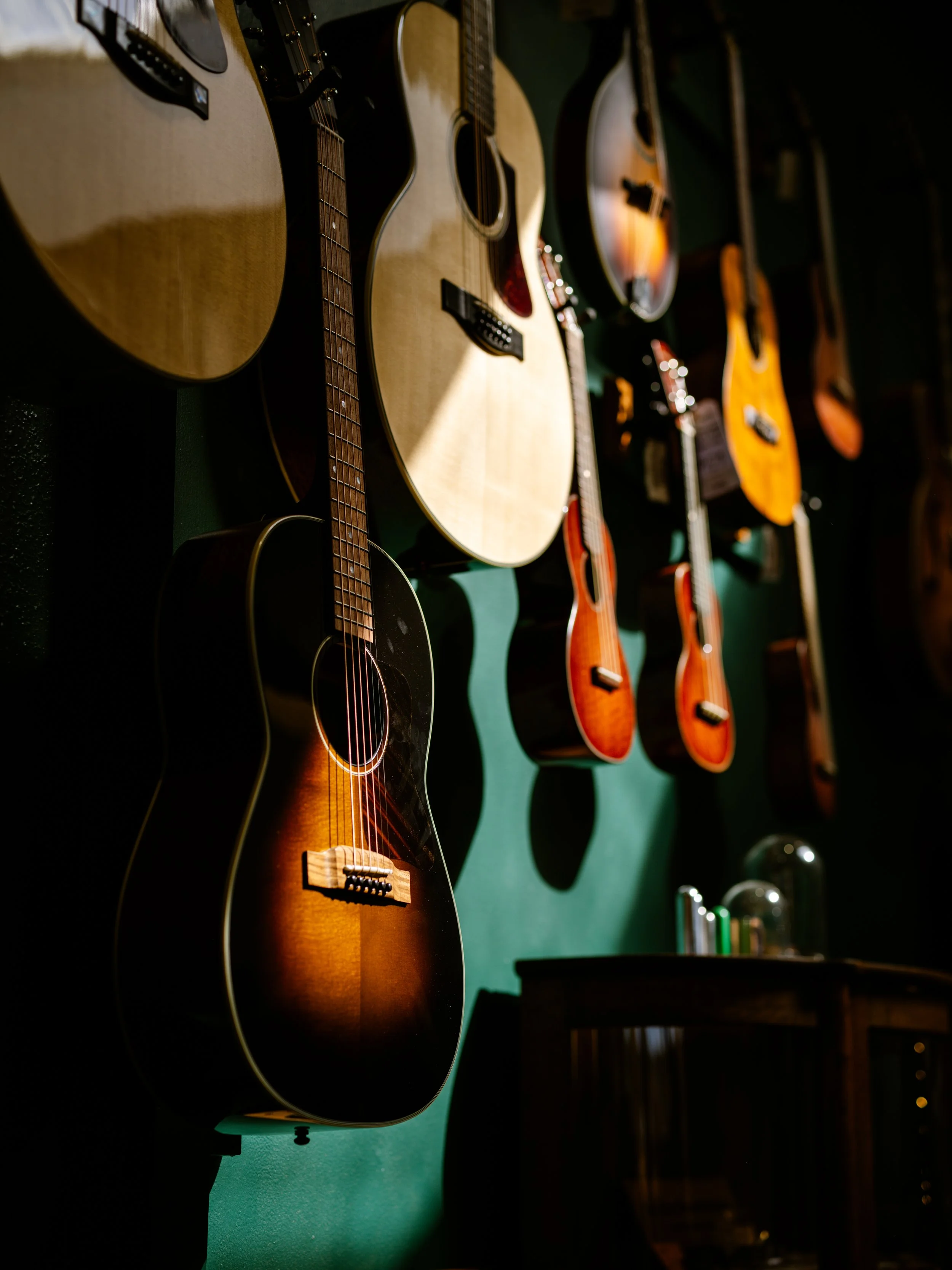 Multiple guitars hanging on a dark wall, with a focus on a sunburst acoustic guitar in the foreground.