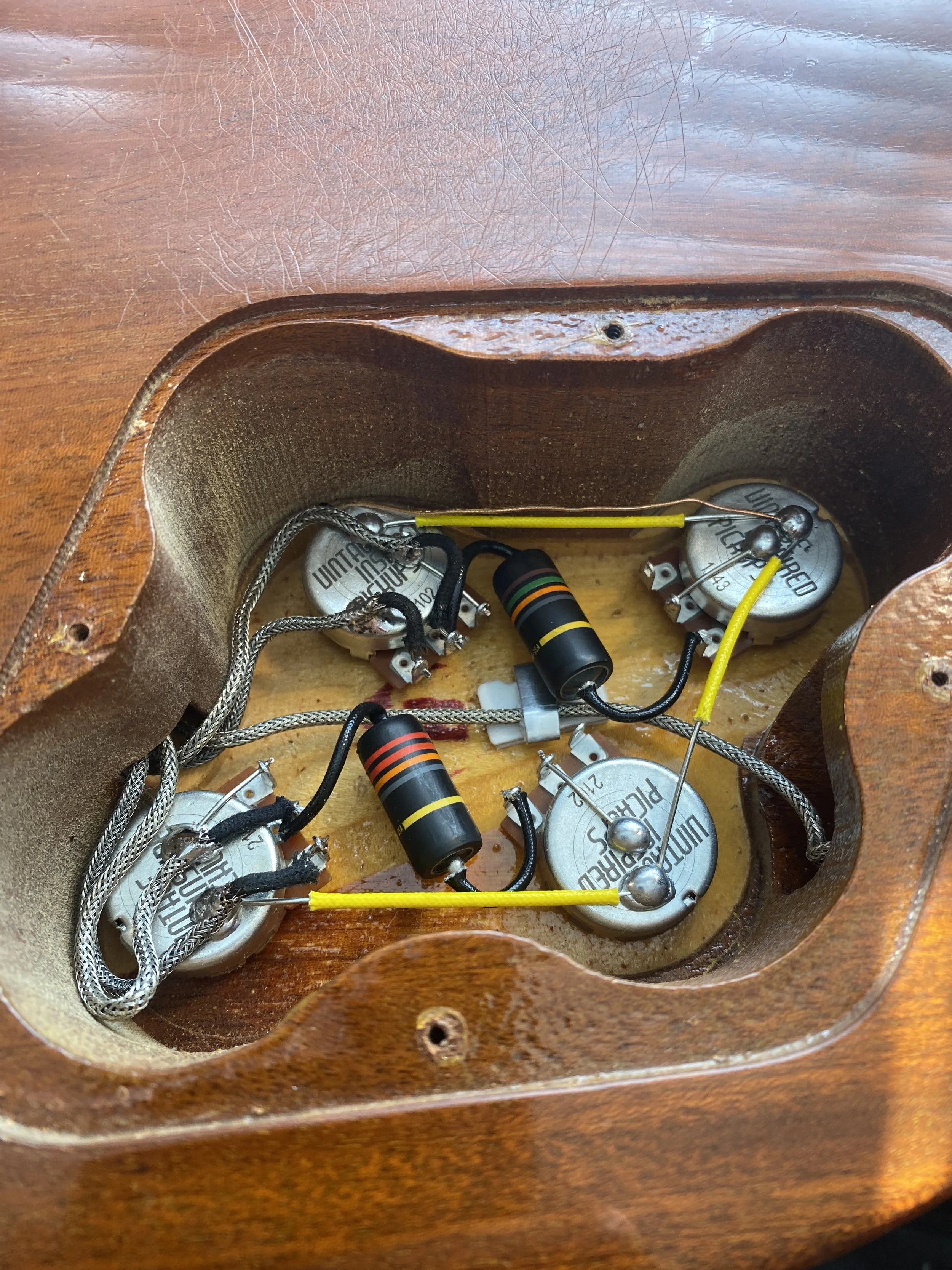 Inside of an acoustic guitar cavity showing wiring, potentiometers, and resistors.